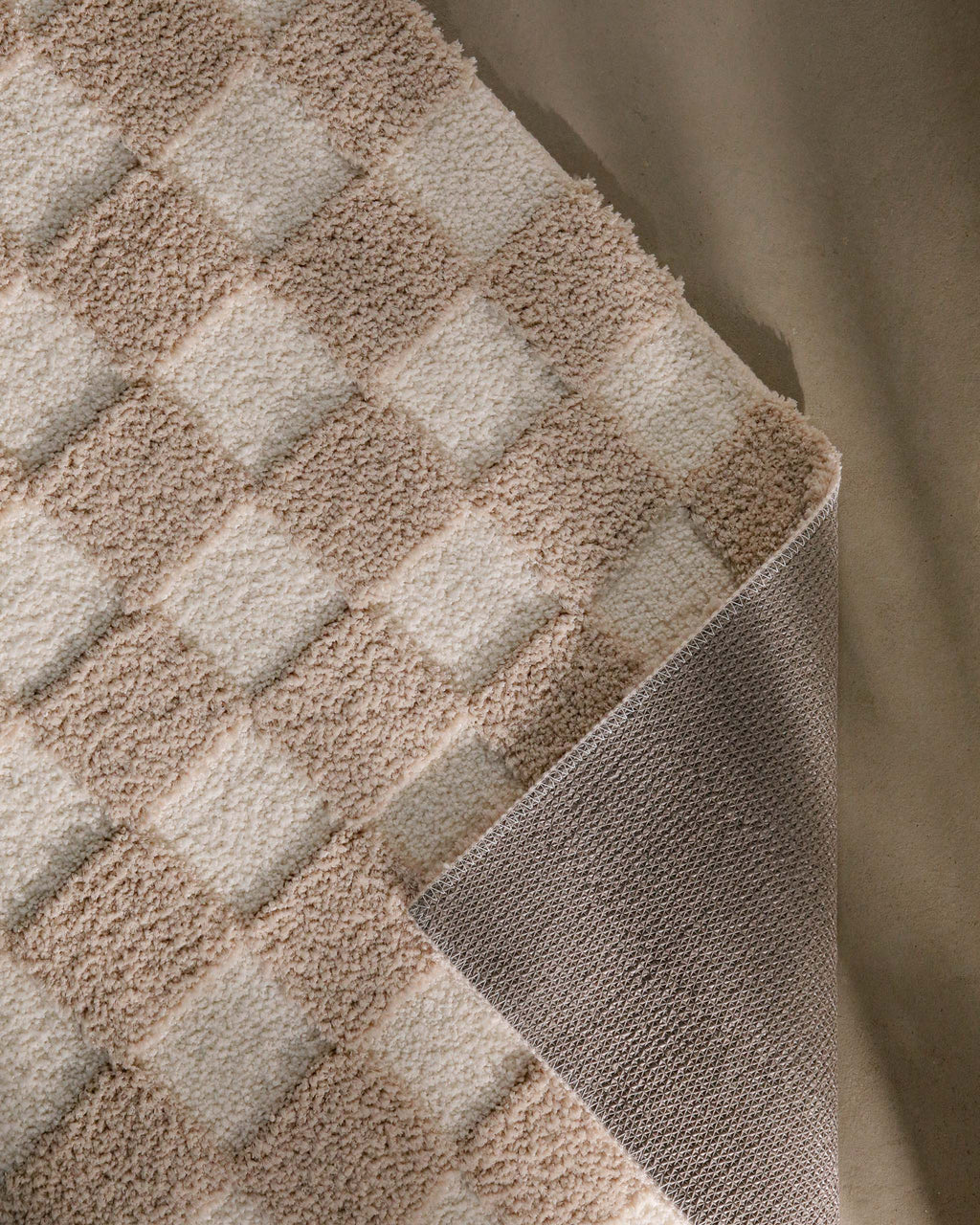 Badteppich von BathKing by WECONhome Bobbi Beige im Badezimmer vor Holzbank auf hellem Boden, rechteckige Matte mit Schachbrettmuster