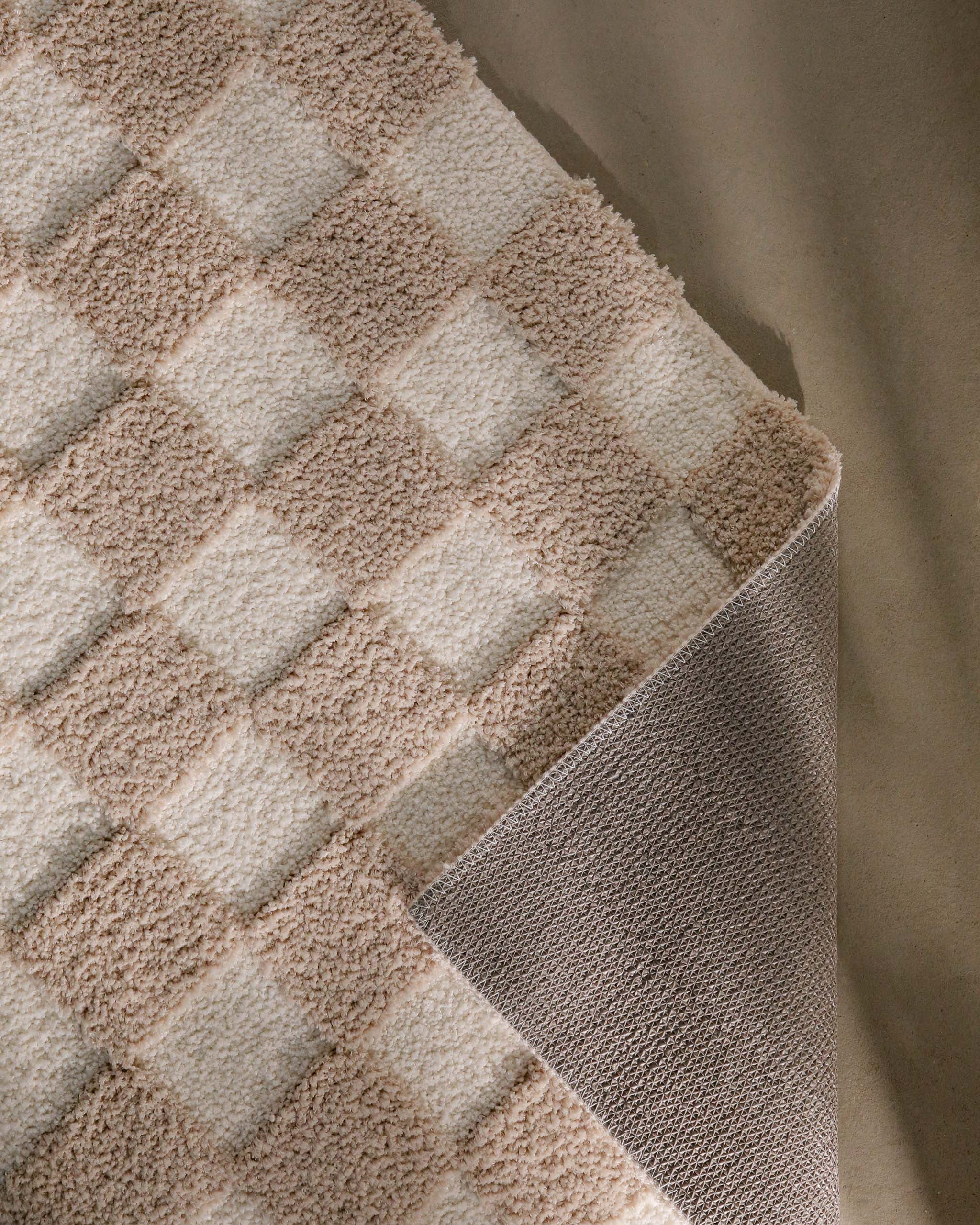 Badteppich von BathKing by WECONhome Bobbi Beige im Badezimmer vor Holzbank auf hellem Boden, rechteckige Matte mit Schachbrettmuster