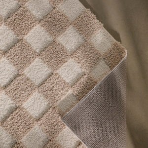 {"class" => "product-thumbnails__image", "alt" => "Badteppich von BathKing by WECONhome Bobbi Beige im Badezimmer vor Holzbank auf hellem Boden, rechteckige Matte mit Schachbrettmuster"}