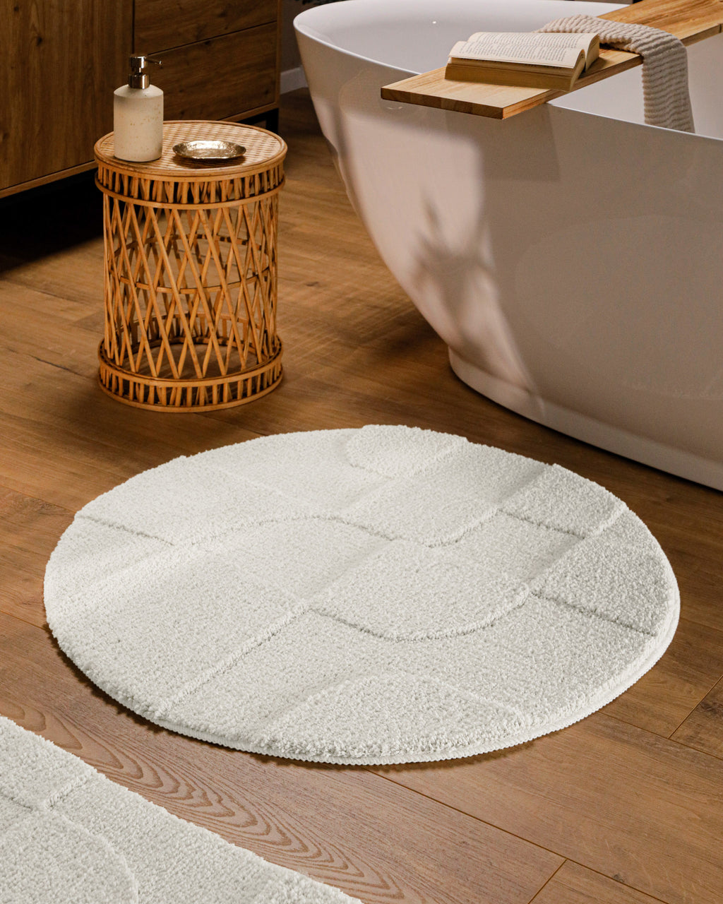 Runder Badteppich von BathKing by WECONhome Davie Weiß im Badezimmer vor Badewanne auf Holzboden, strukturiertes Linienrelief im Flor sichtbar