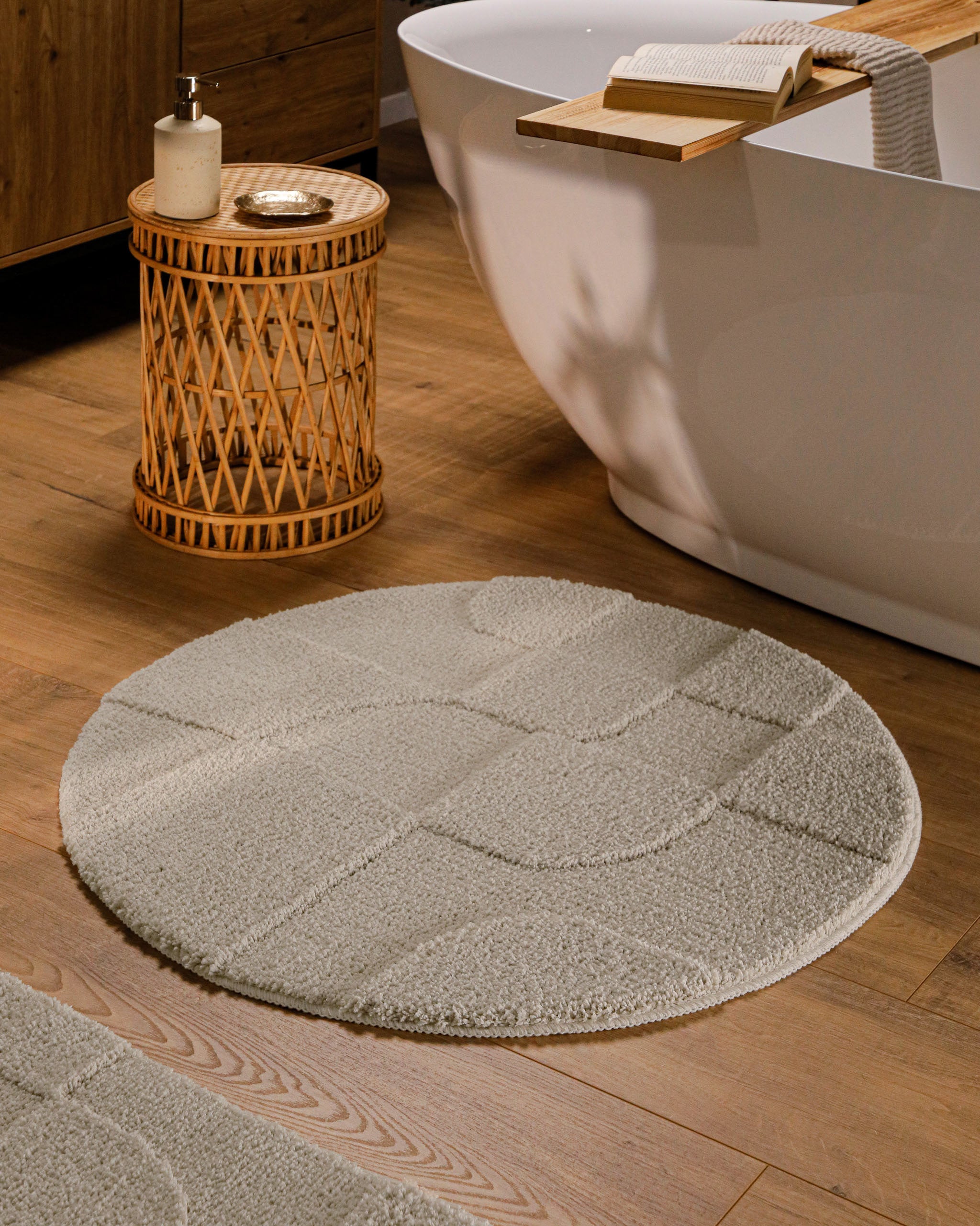 Runder Badteppich von BathKing by WECONhome Davie Grau im Badezimmer vor Badewanne auf Holzboden, strukturiertes Linienrelief im Flor sichtbar