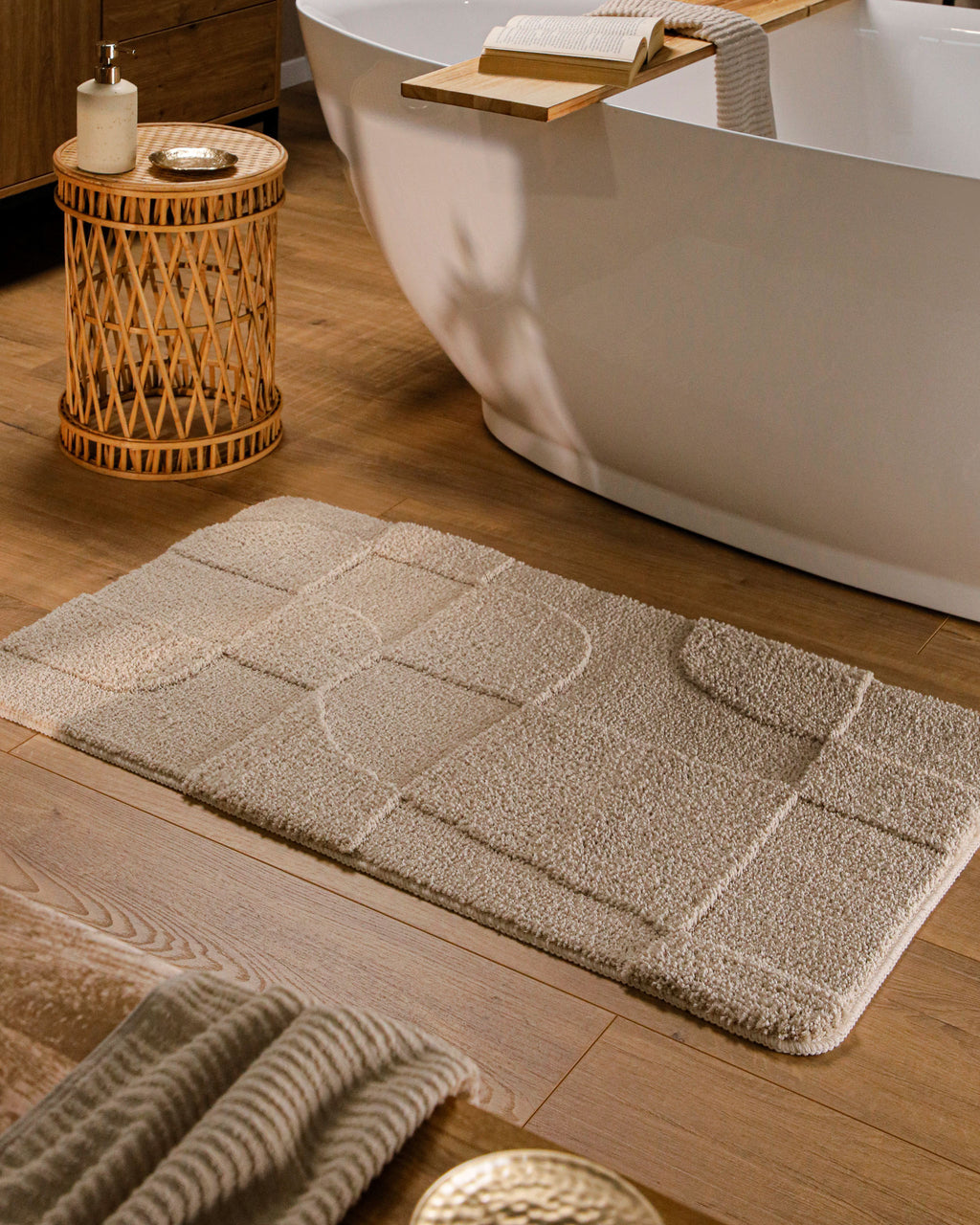 Badteppich von BathKing by WECONhome Davie Sand Beige rechteckig im Badezimmer vor Badewanne auf Holzboden liegend, Strukturmuster im Flor sichtbar