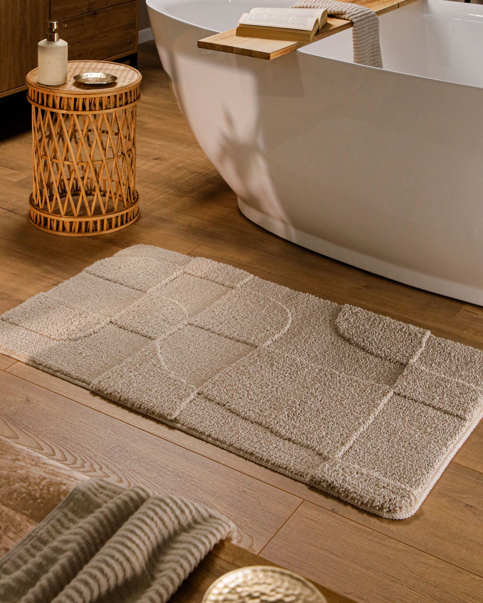 Badteppich von BathKing by WECONhome Davie Sand Beige rechteckig im Badezimmer vor Badewanne auf Holzboden liegend, Strukturmuster im Flor sichtbar