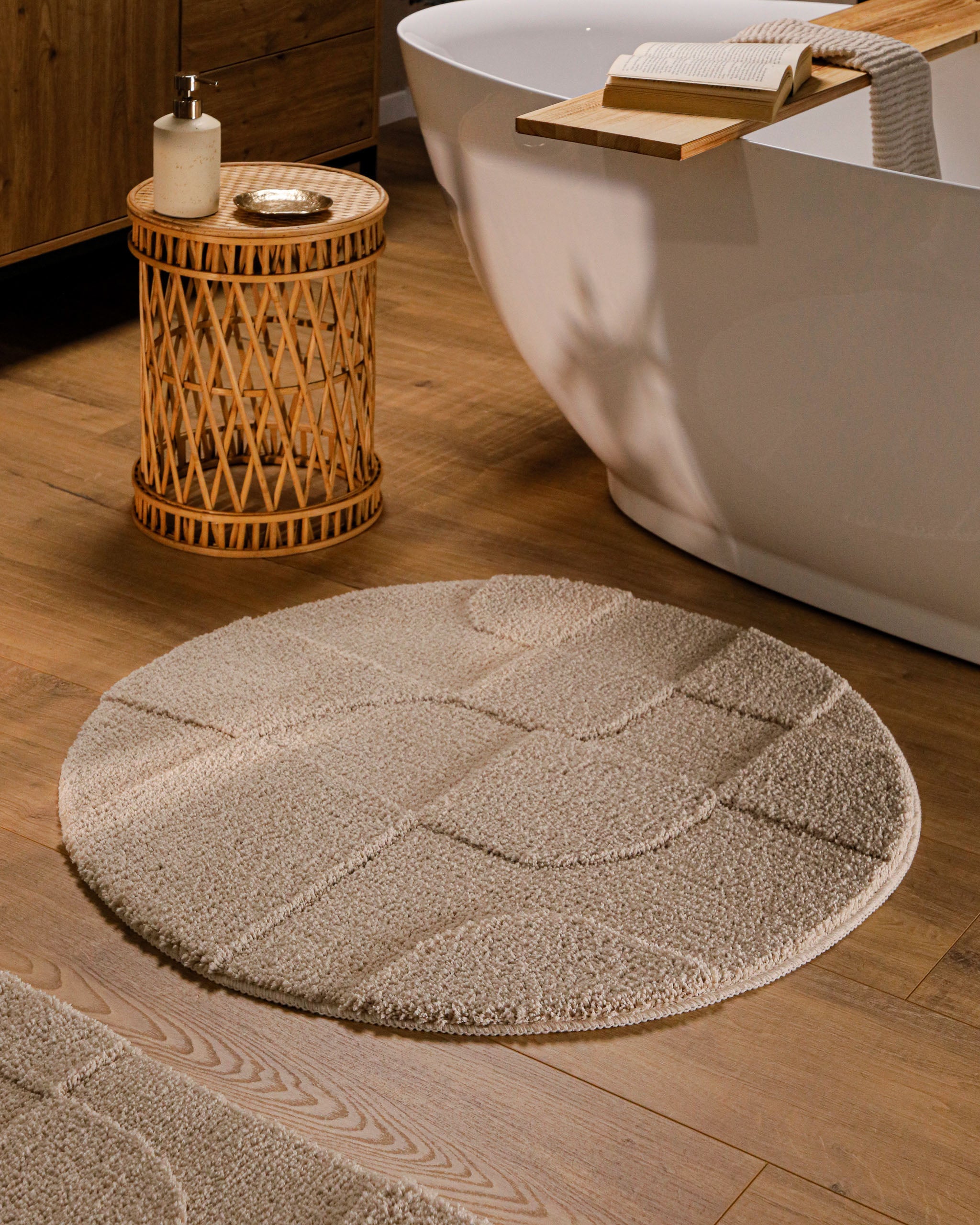 Runder Badteppich von BathKing by WECONhome Davie Sand Beige im Badezimmer vor Badewanne auf Holzboden, strukturiertes Linienrelief im Flor sichtbar