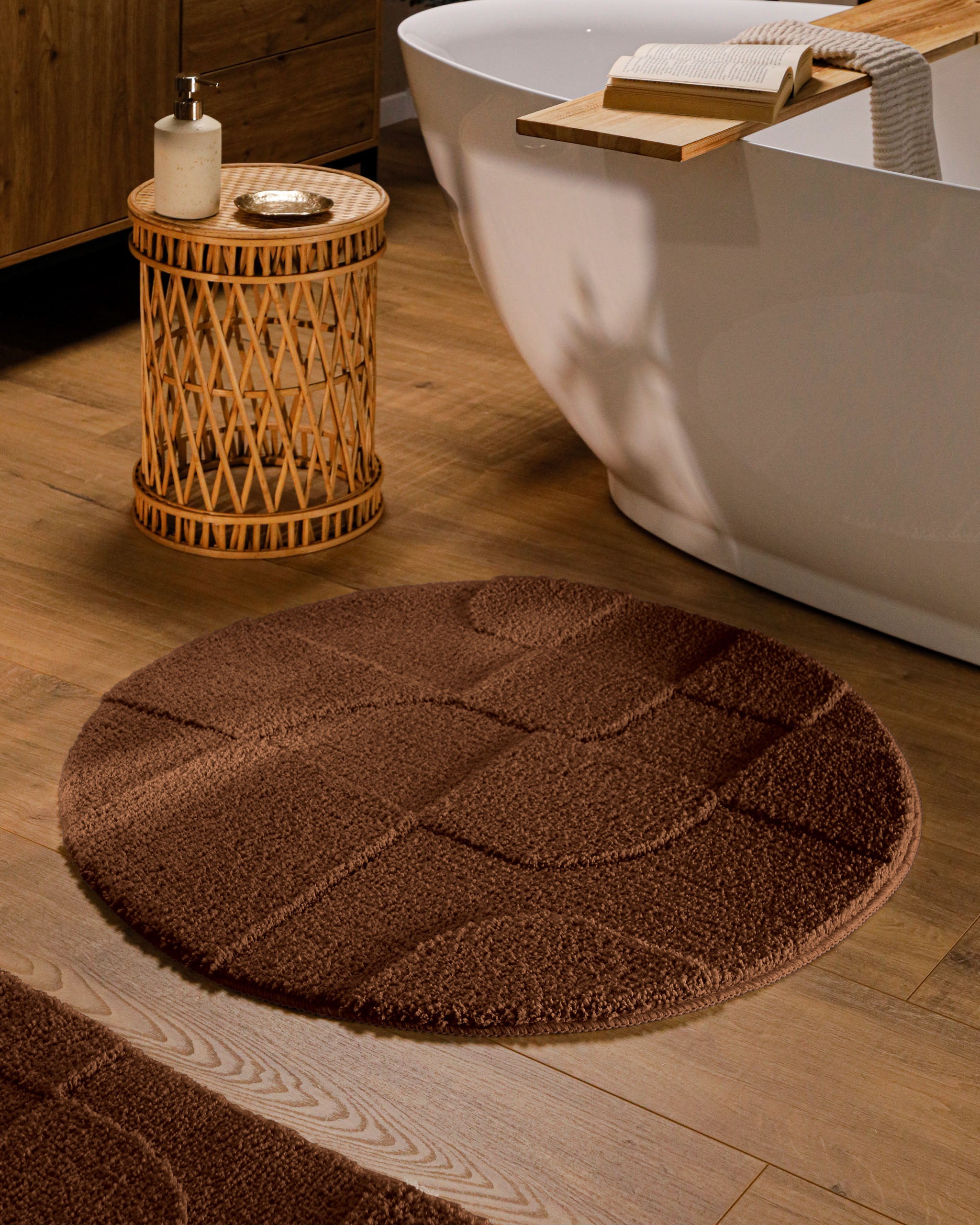 Runder Badteppich von BathKing by WECONhome Davie Braun im Badezimmer vor Badewanne auf Holzboden, strukturiertes Linienrelief im Flor sichtbar