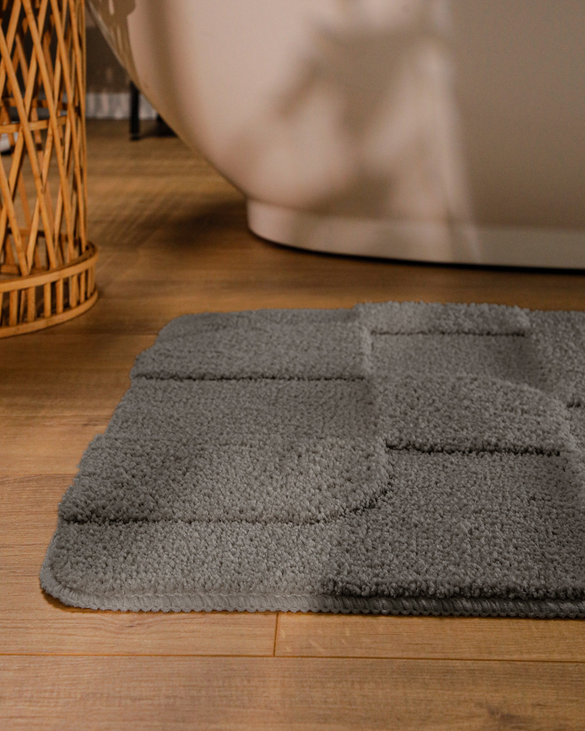 Badteppich von BathKing by WECONhome Davie Basalt Grau runde Matte im Badezimmer vor Badewanne, Strukturmuster im Flor auf Holzboden sichtbar