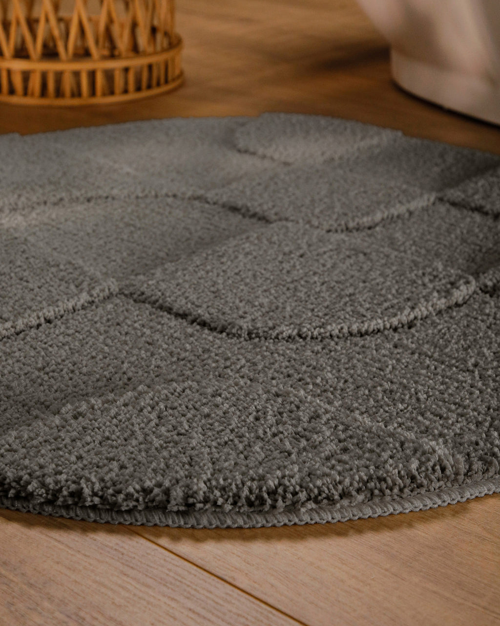 Badteppich von BathKing by WECONhome Davie Basalt Grau rund im Badezimmer auf Holzboden neben Badewanne, Florstruktur und Linienrelief erkennbar
