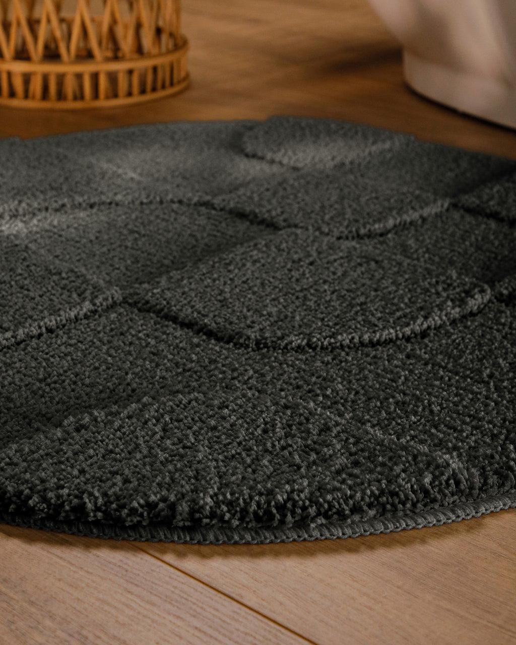 Badteppich von BathKing by WECONhome Davie Anthrazit Grau rund im Badezimmer auf Holzboden neben Badewanne, Florstruktur und Linienrelief erkennbar