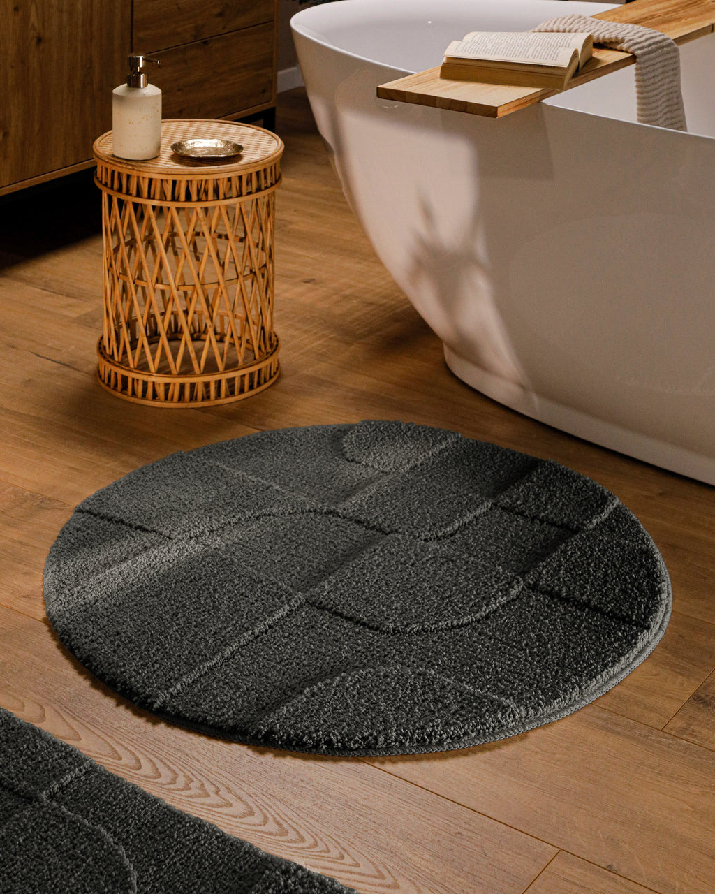 Runder Badteppich von BathKing by WECONhome Davie Anthrazit Grau im Badezimmer vor Badewanne auf Holzboden, strukturiertes Linienrelief im Flor sichtbar