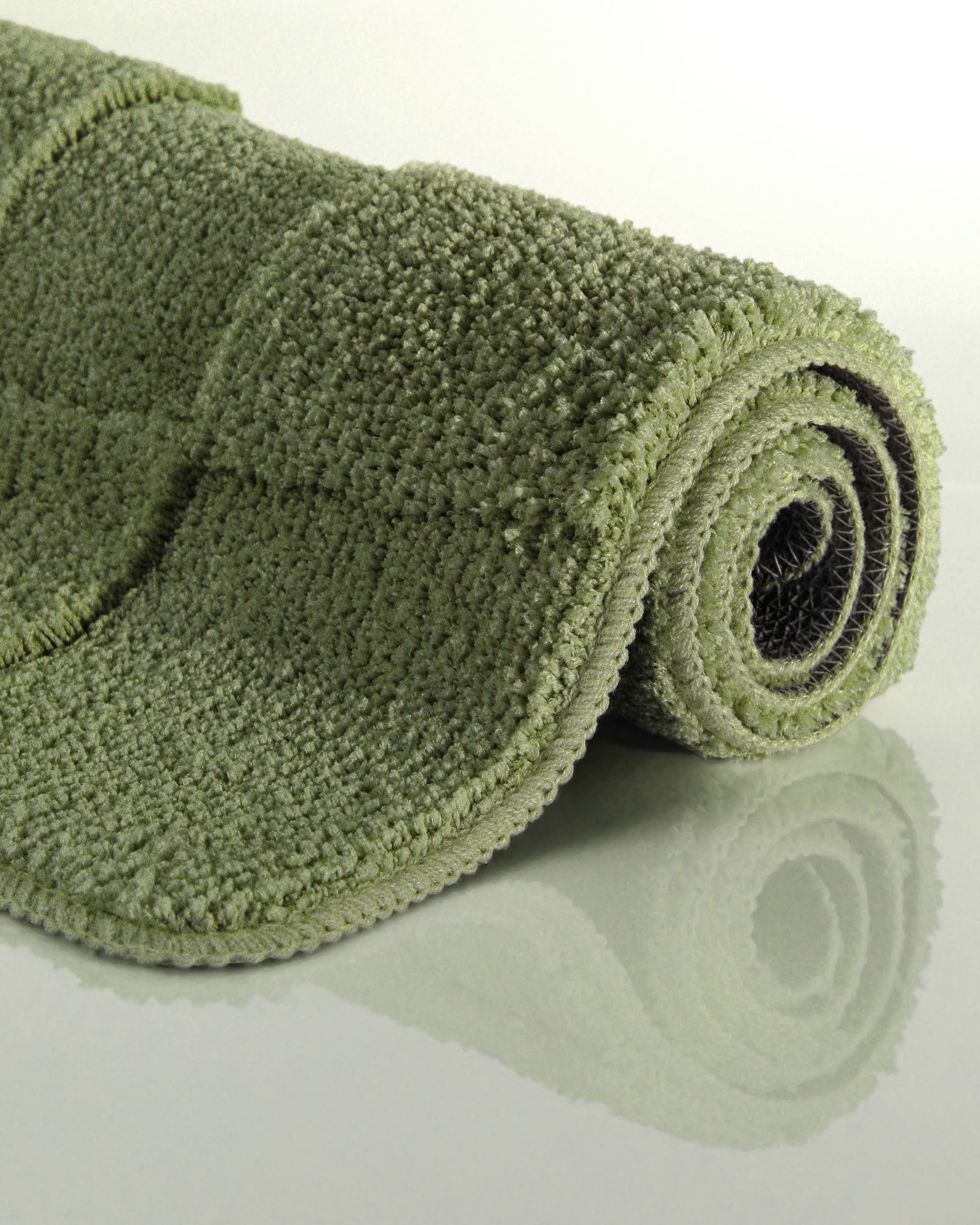Badteppich von BathKing by WECONhome Davie Reseda Grün aufgerollt auf hellem Hintergrund, Seitenansicht zeigt Florhöhe und Teppichkante
