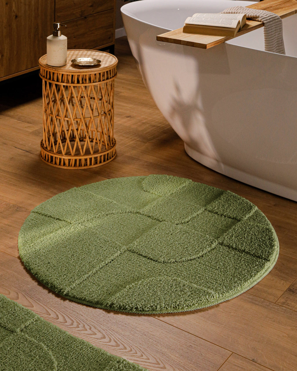 Runder Badteppich von BathKing by WECONhome Davie Reseda Grün im Badezimmer vor Badewanne auf Holzboden, strukturiertes Linienrelief im Flor sichtbar