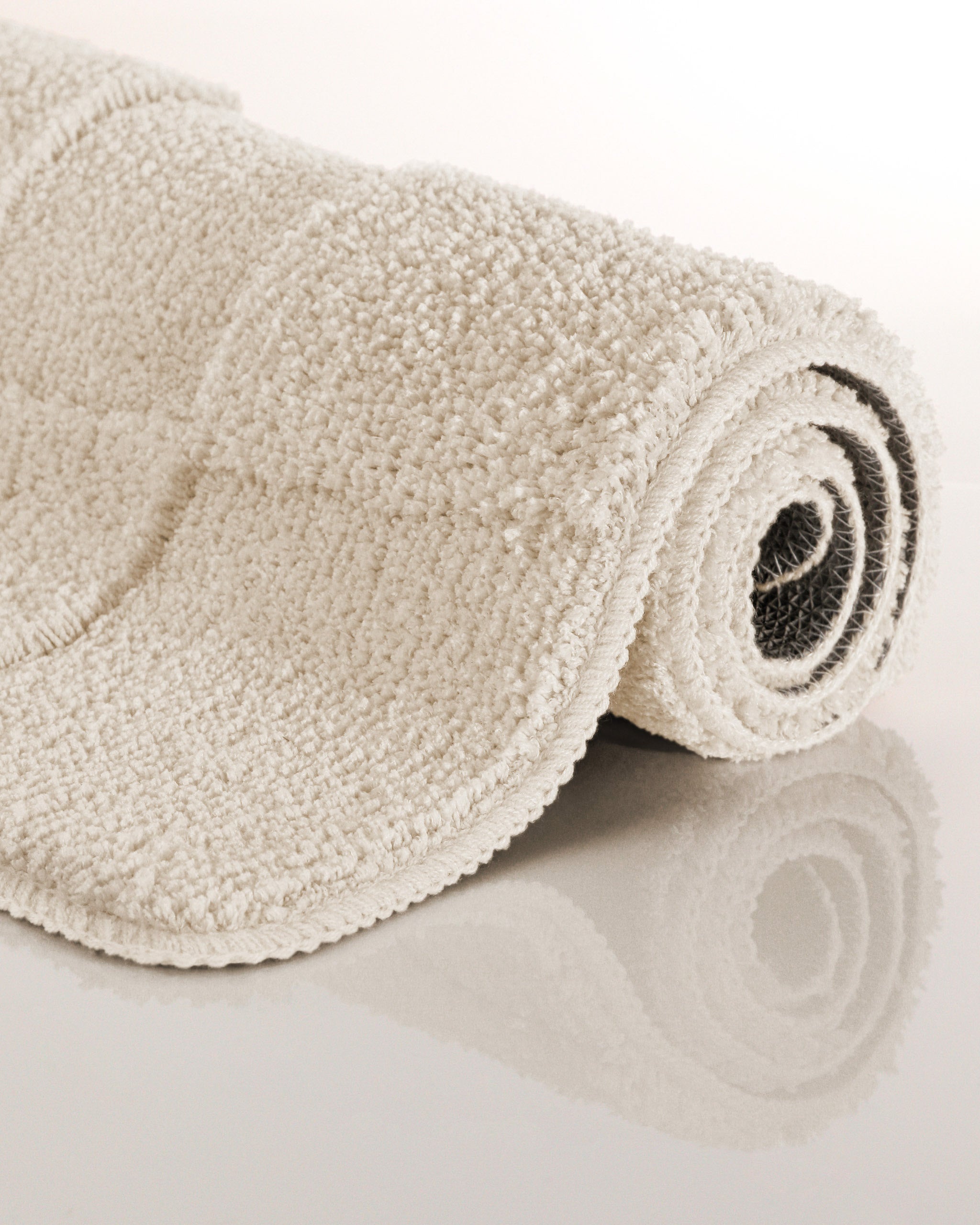 Badteppich von BathKing by WECONhome Davie Creme Weiß aufgerollt auf hellem Hintergrund, Seitenansicht zeigt Florhöhe und Teppichkante