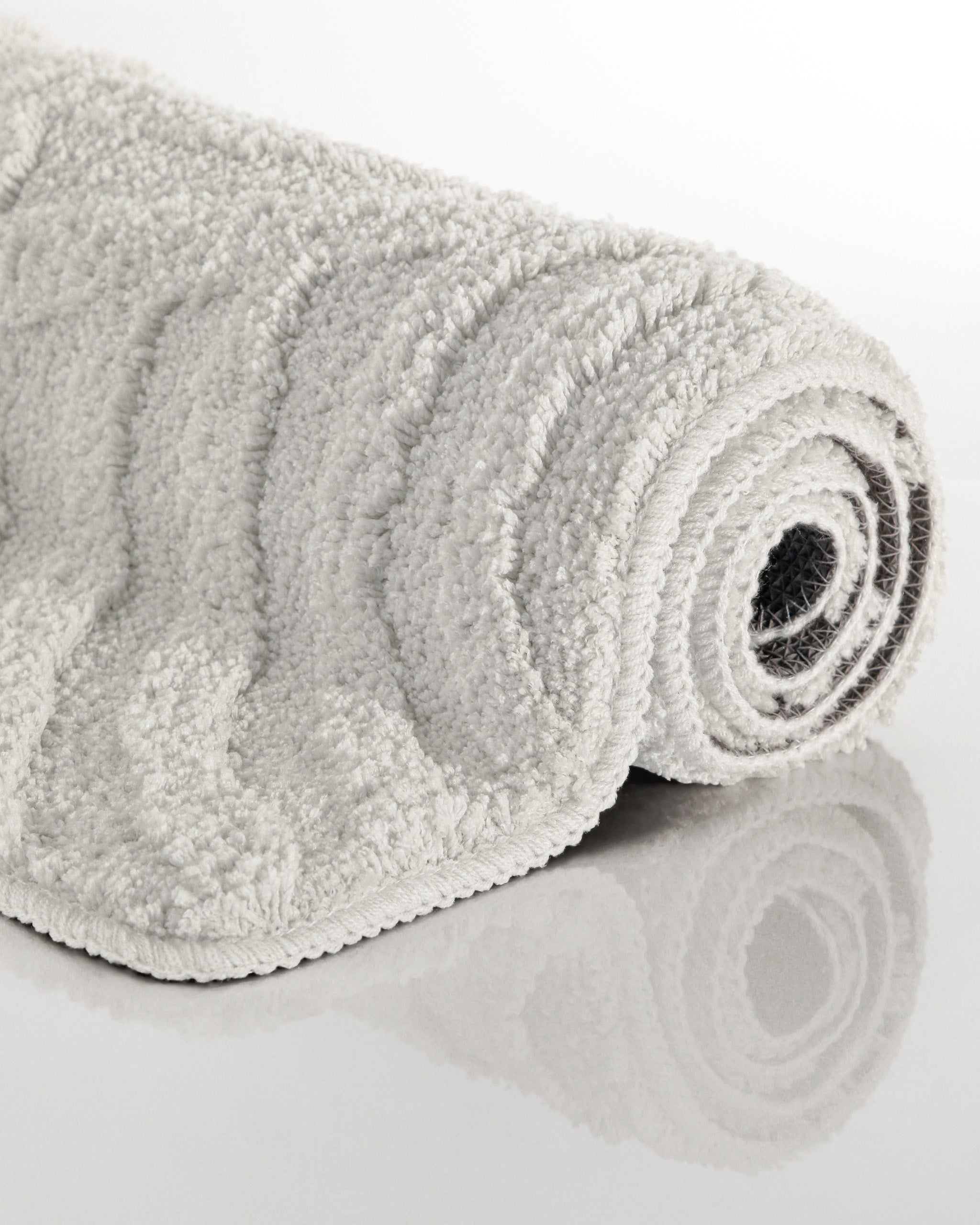 Badteppich von BathKing by WECONhome Fiete Weiß aufgerollt auf hellem Hintergrund, Seitenansicht zeigt Florhöhe und Teppichkante
