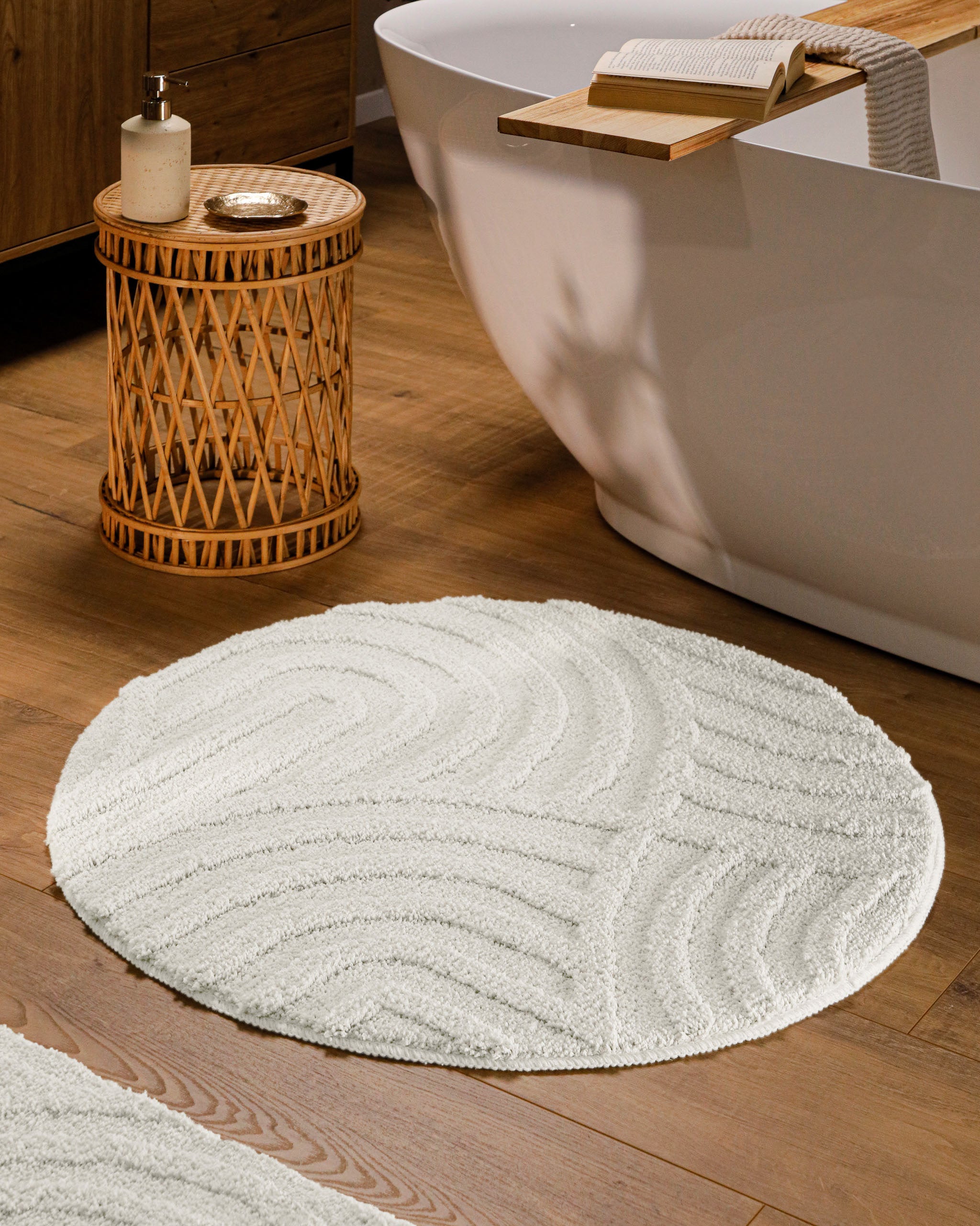 Runder Badteppich von BathKing by WECONhome Fiete Weiß im Badezimmer vor Badewanne auf Holzboden, strukturiertes Linienrelief im Flor sichtbar