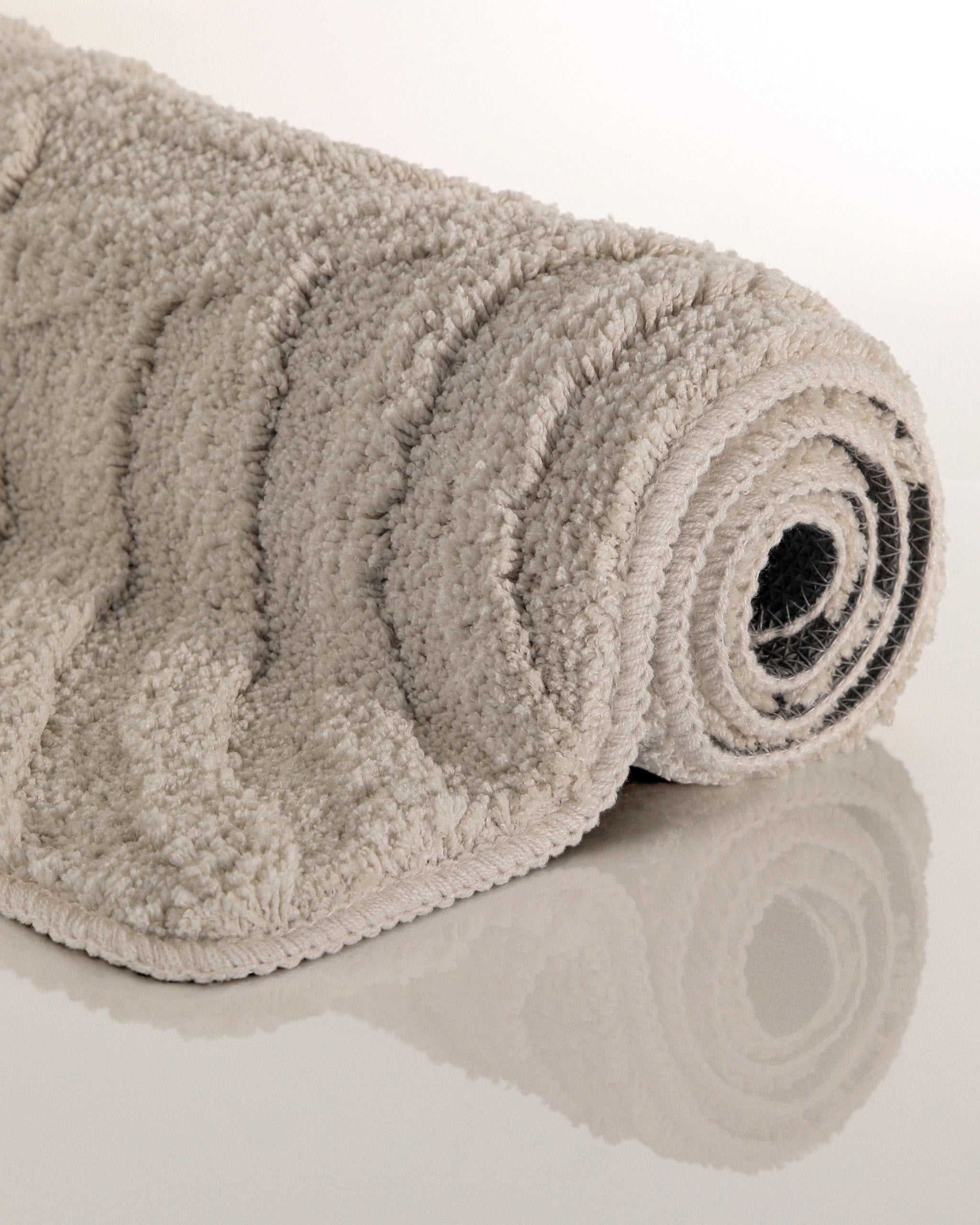 Badteppich von BathKing by WECONhome Fiete Grau aufgerollt auf hellem Hintergrund, Seitenansicht zeigt Florhöhe und Teppichkante