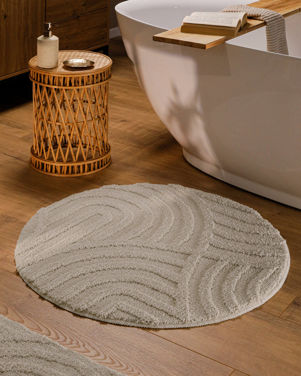 Runder Badteppich von BathKing by WECONhome Fiete Grau im Badezimmer vor Badewanne auf Holzboden, strukturiertes Linienrelief im Flor sichtbar