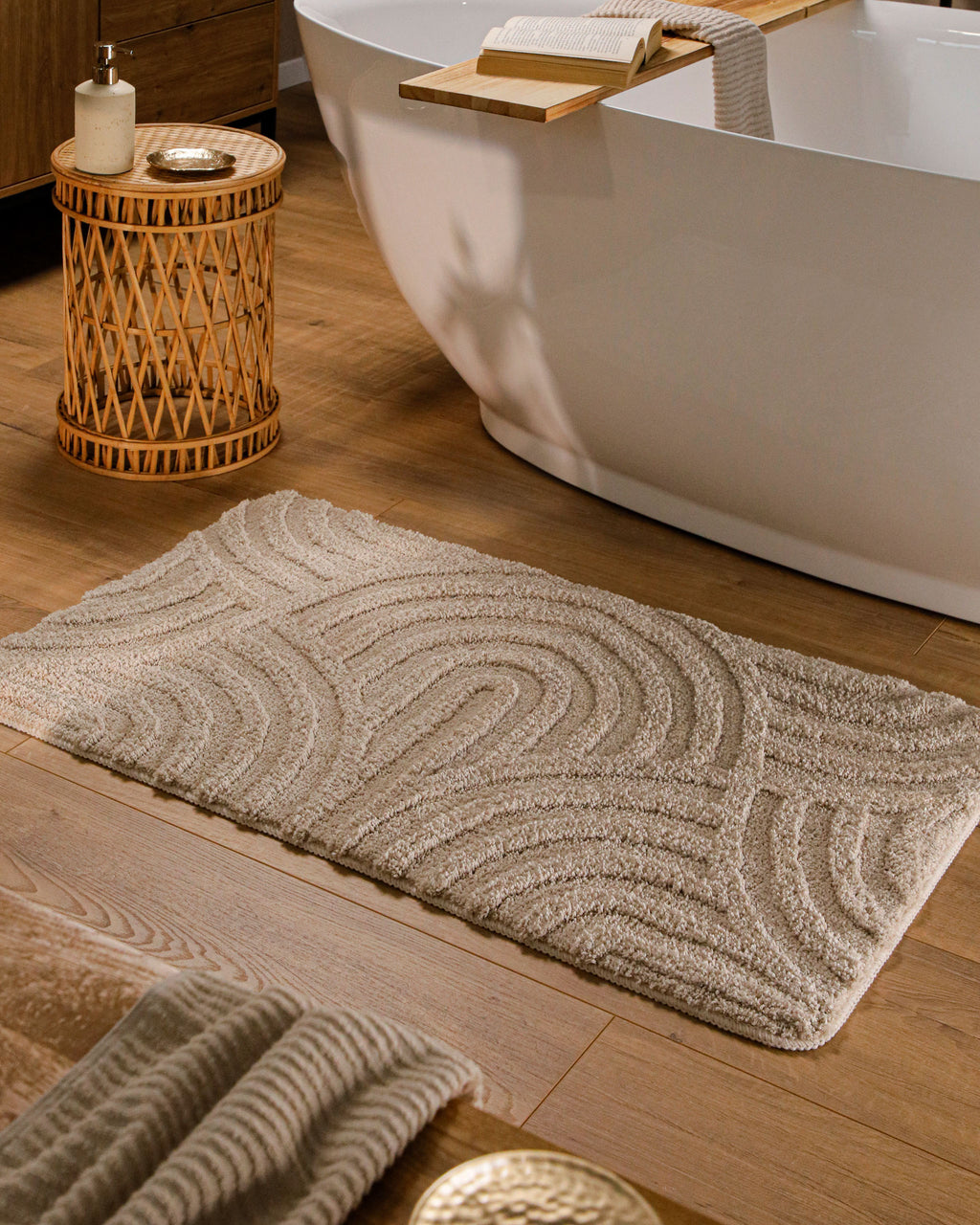 Badteppich von BathKing by WECONhome Fiete Sand Beige rechteckig im Badezimmer vor Badewanne auf Holzboden liegend, Strukturmuster im Flor sichtbar