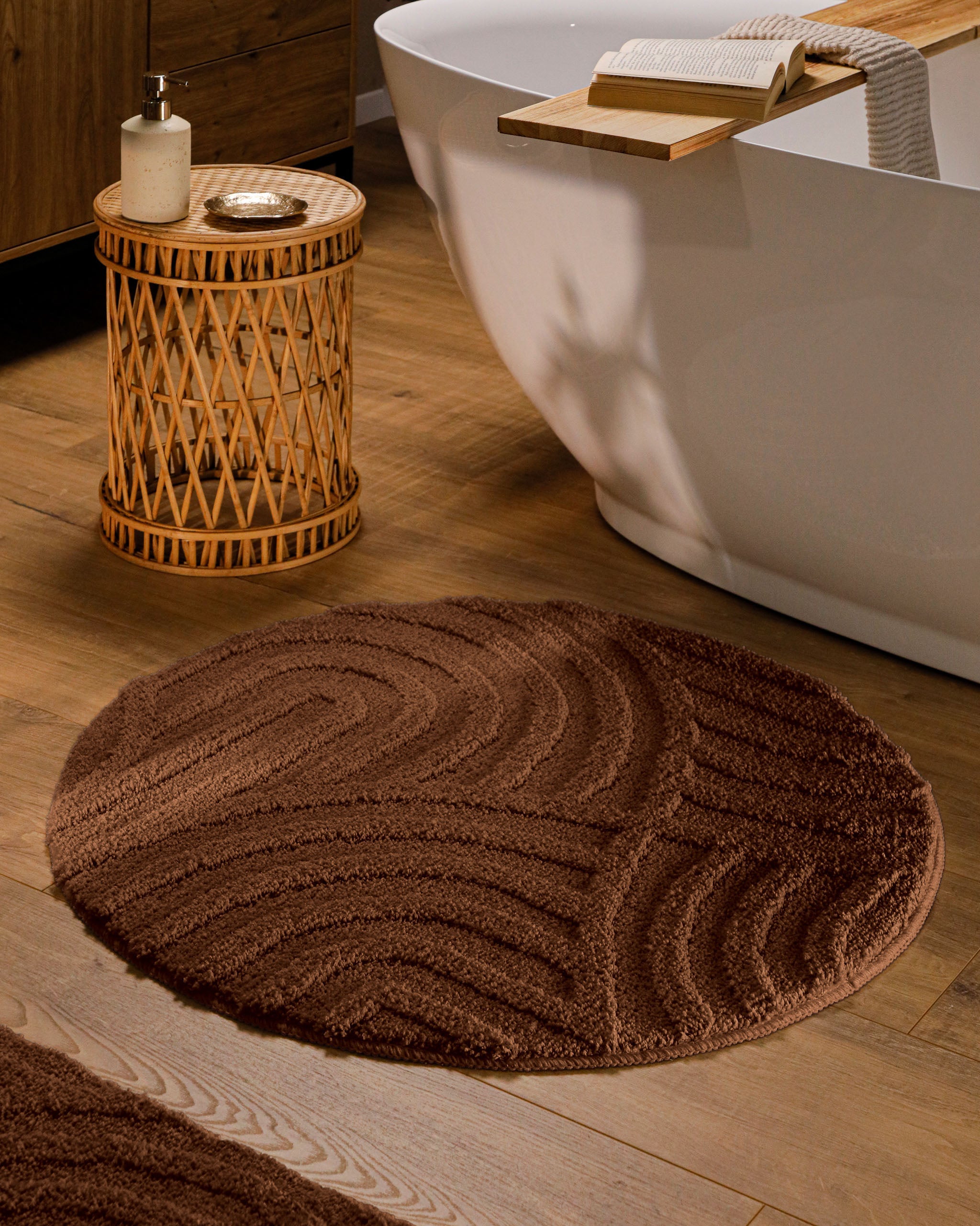 Runder Badteppich von BathKing by WECONhome Fiete Braun im Badezimmer vor Badewanne auf Holzboden, strukturiertes Linienrelief im Flor sichtbar