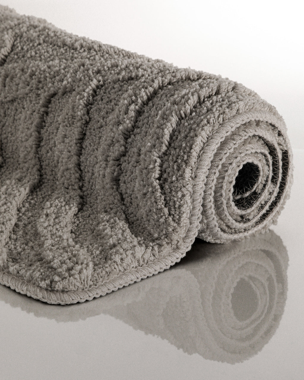 Badteppich von BathKing by WECONhome Fiete Basalt Grau aufgerollt auf hellem Hintergrund, Seitenansicht zeigt Florhöhe und Teppichkante