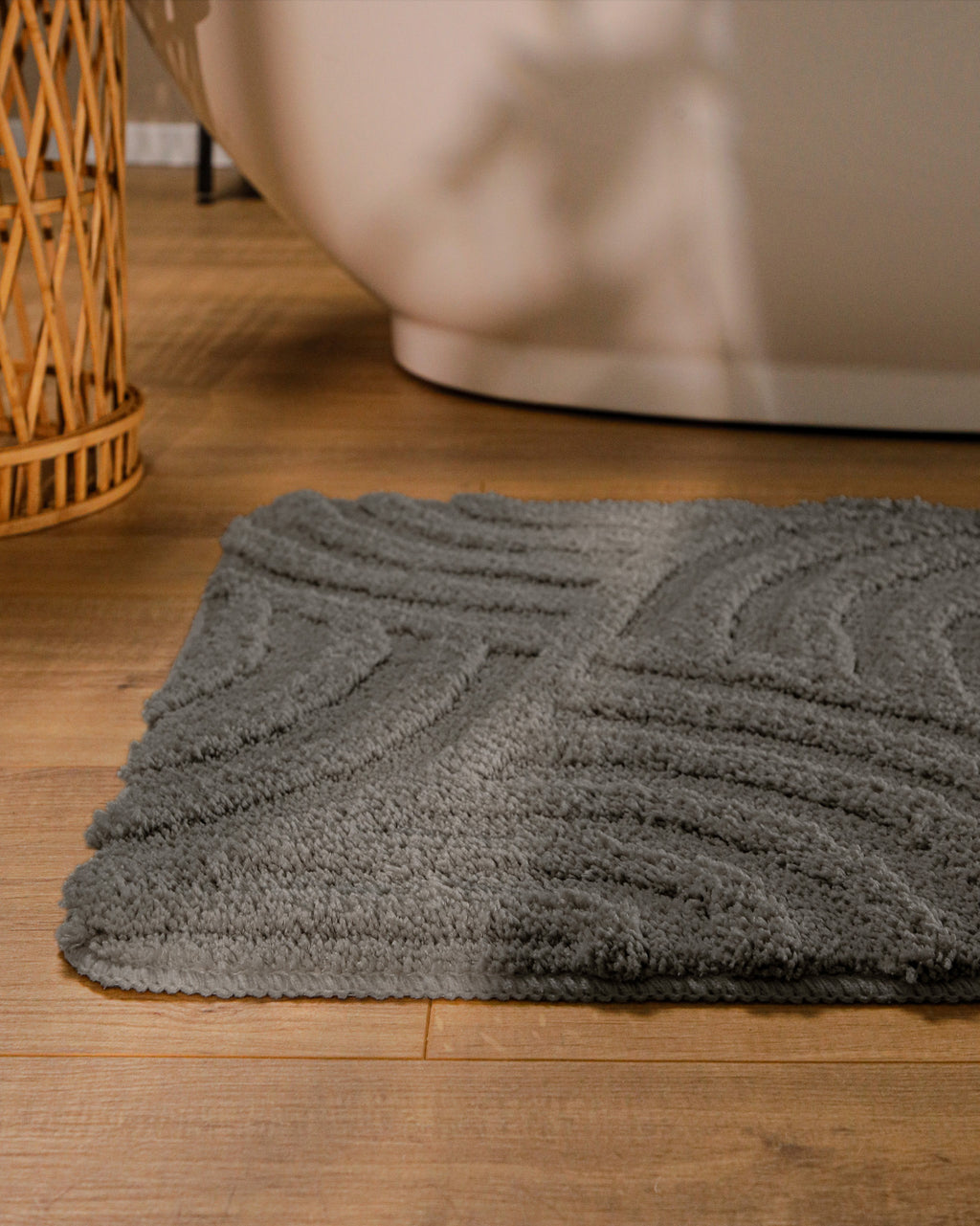 Badteppich von BathKing by WECONhome Fiete Basalt Grau runde Matte im Badezimmer vor Badewanne, Strukturmuster im Flor auf Holzboden sichtbar