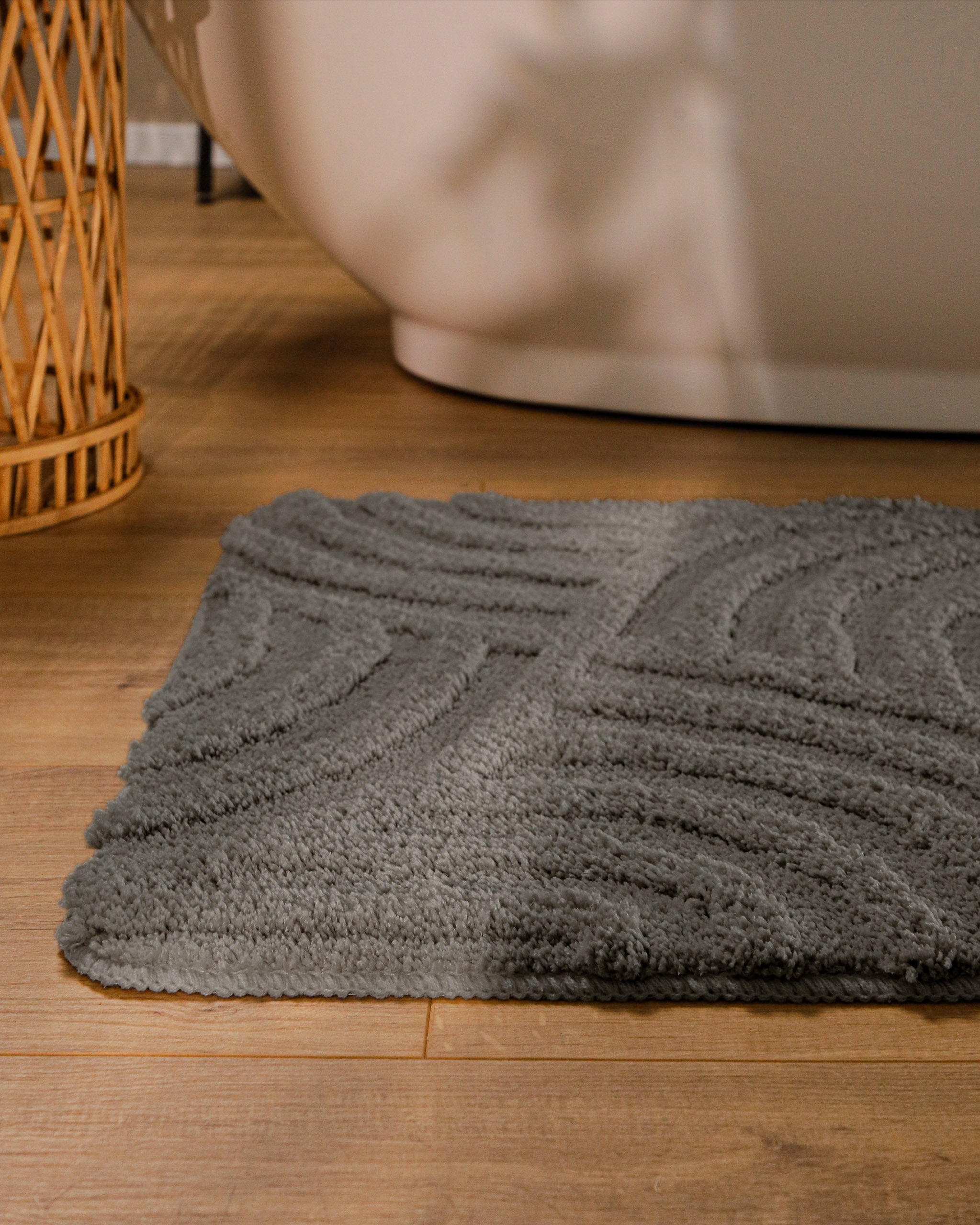 Badteppich von BathKing by WECONhome Fiete Basalt Grau runde Matte im Badezimmer vor Badewanne, Strukturmuster im Flor auf Holzboden sichtbar