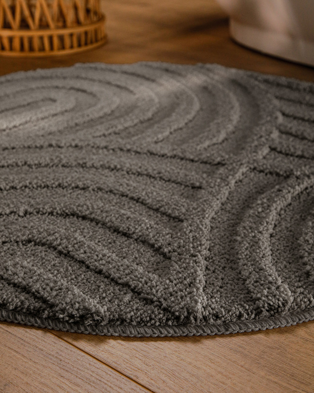Badteppich von BathKing by WECONhome Fiete Basalt Grau rund im Badezimmer auf Holzboden neben Badewanne, Florstruktur und Linienrelief erkennbar