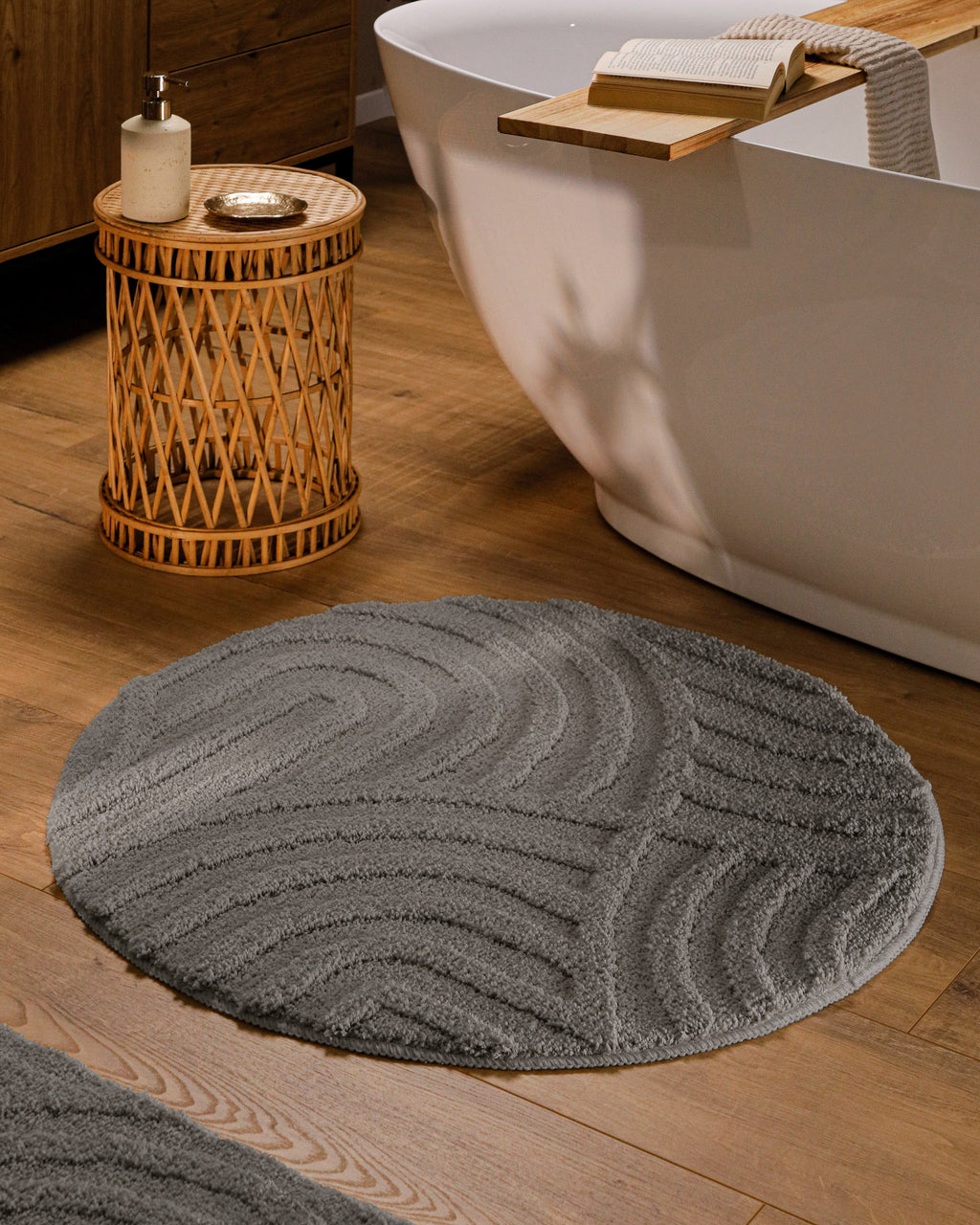 Runder Badteppich von BathKing by WECONhome Fiete Basalt Grau im Badezimmer vor Badewanne auf Holzboden, strukturiertes Linienrelief im Flor sichtbar