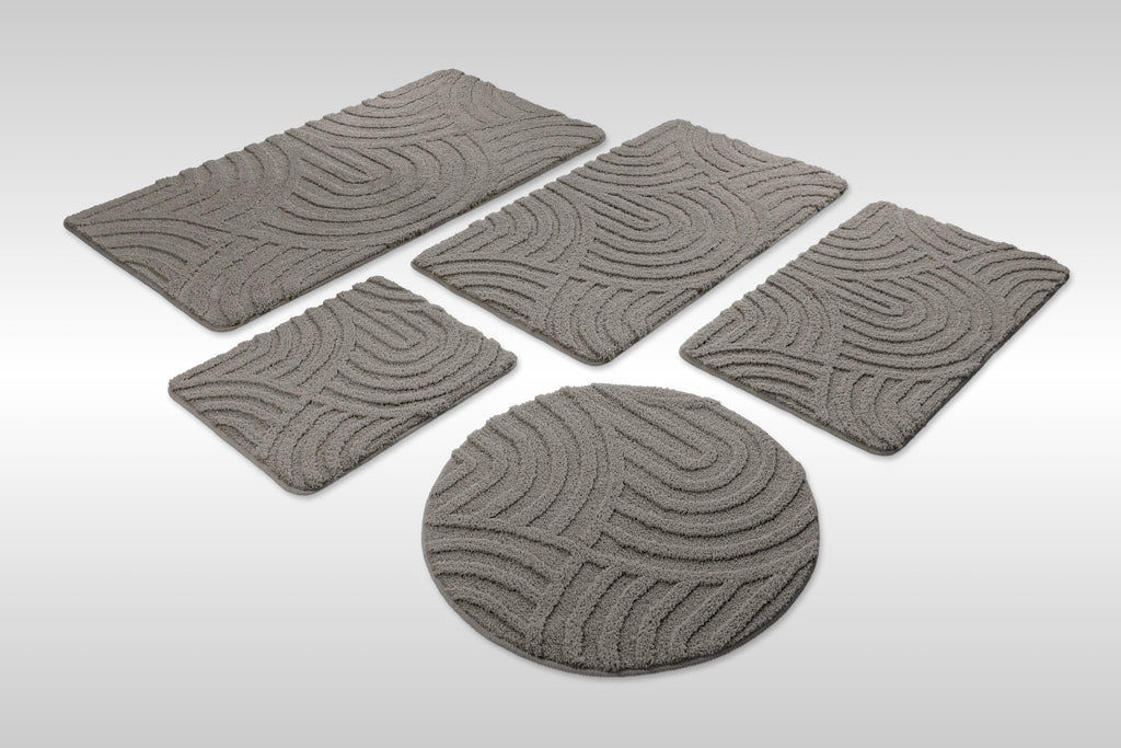 Badteppich von BathKing by WECONhome Fiete Basalt Grau Set aus rechteckigen und runden Badmatten, mehrere Größen auf hellem Hintergrund angeordnet