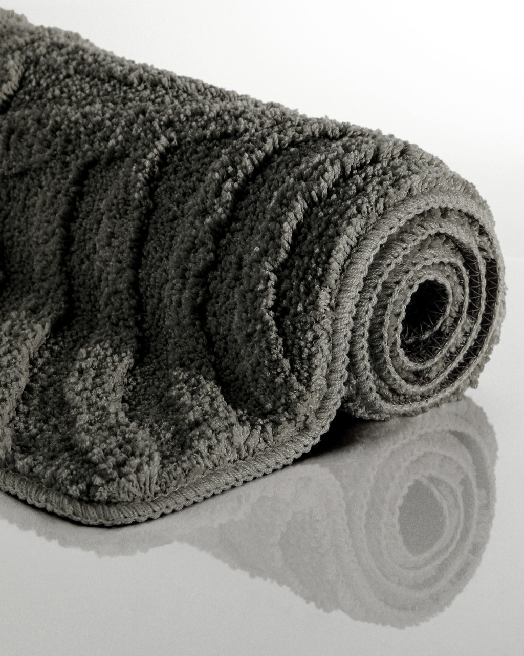 Badteppich von BathKing by WECONhome Fiete Anthrazit Grau aufgerollt auf hellem Hintergrund, Seitenansicht zeigt Florhöhe und Teppichkante