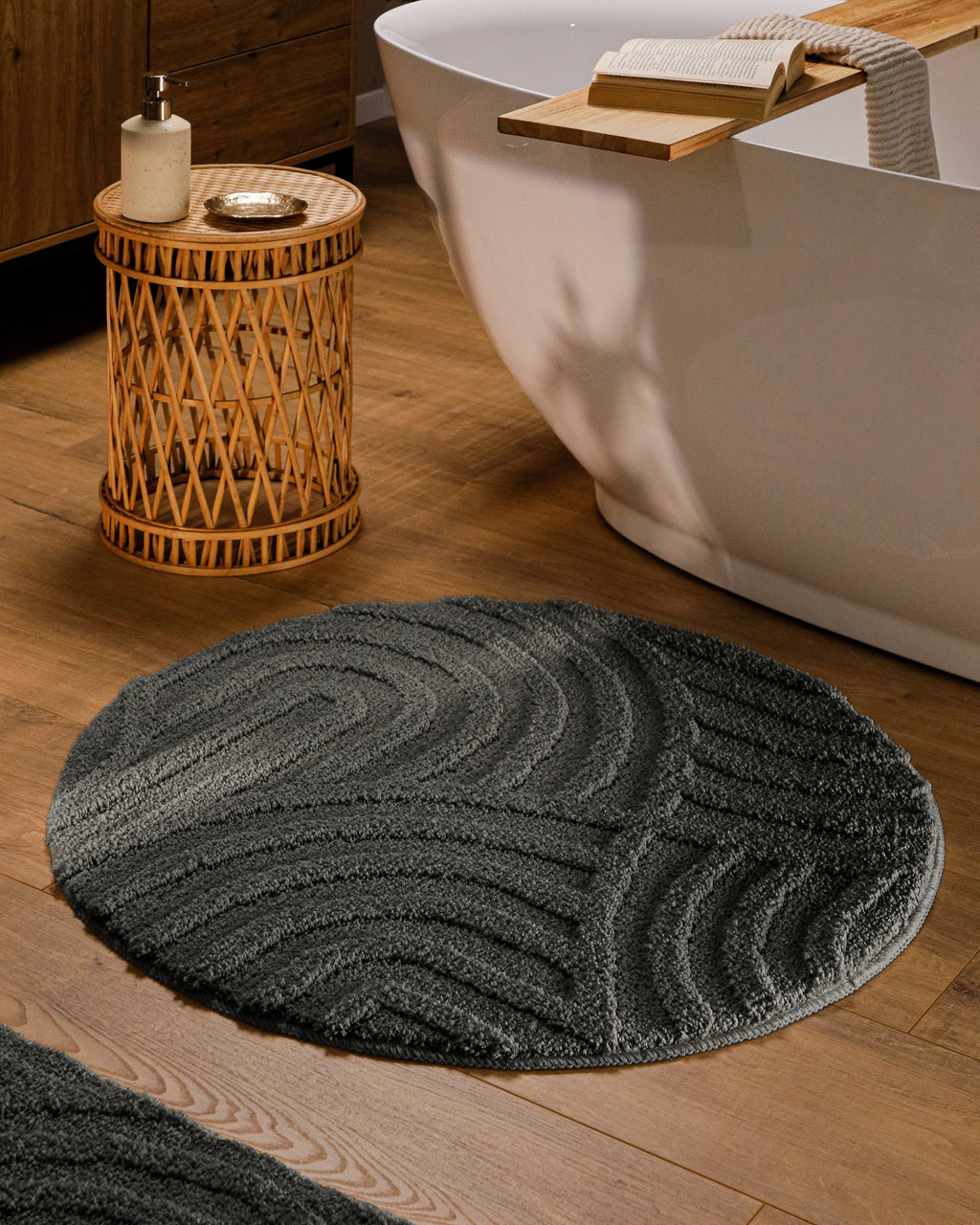 Runder Badteppich von BathKing by WECONhome Fiete Anthrazit Grau im Badezimmer vor Badewanne auf Holzboden, strukturiertes Linienrelief im Flor sichtbar