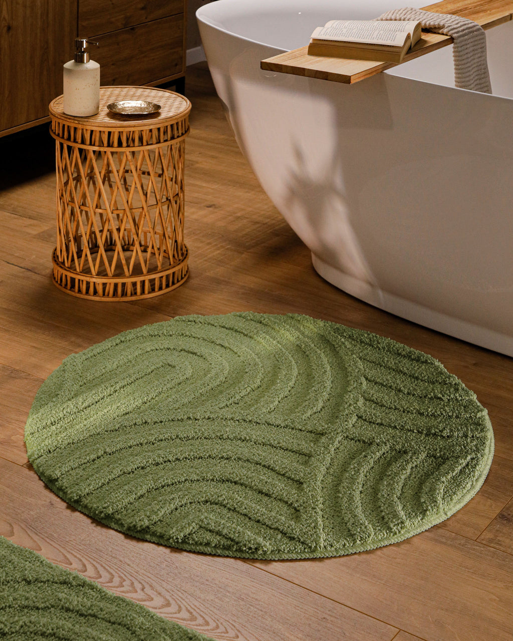 Runder Badteppich von BathKing by WECONhome Fiete Reseda Grün im Badezimmer vor Badewanne auf Holzboden, strukturiertes Linienrelief im Flor sichtbar