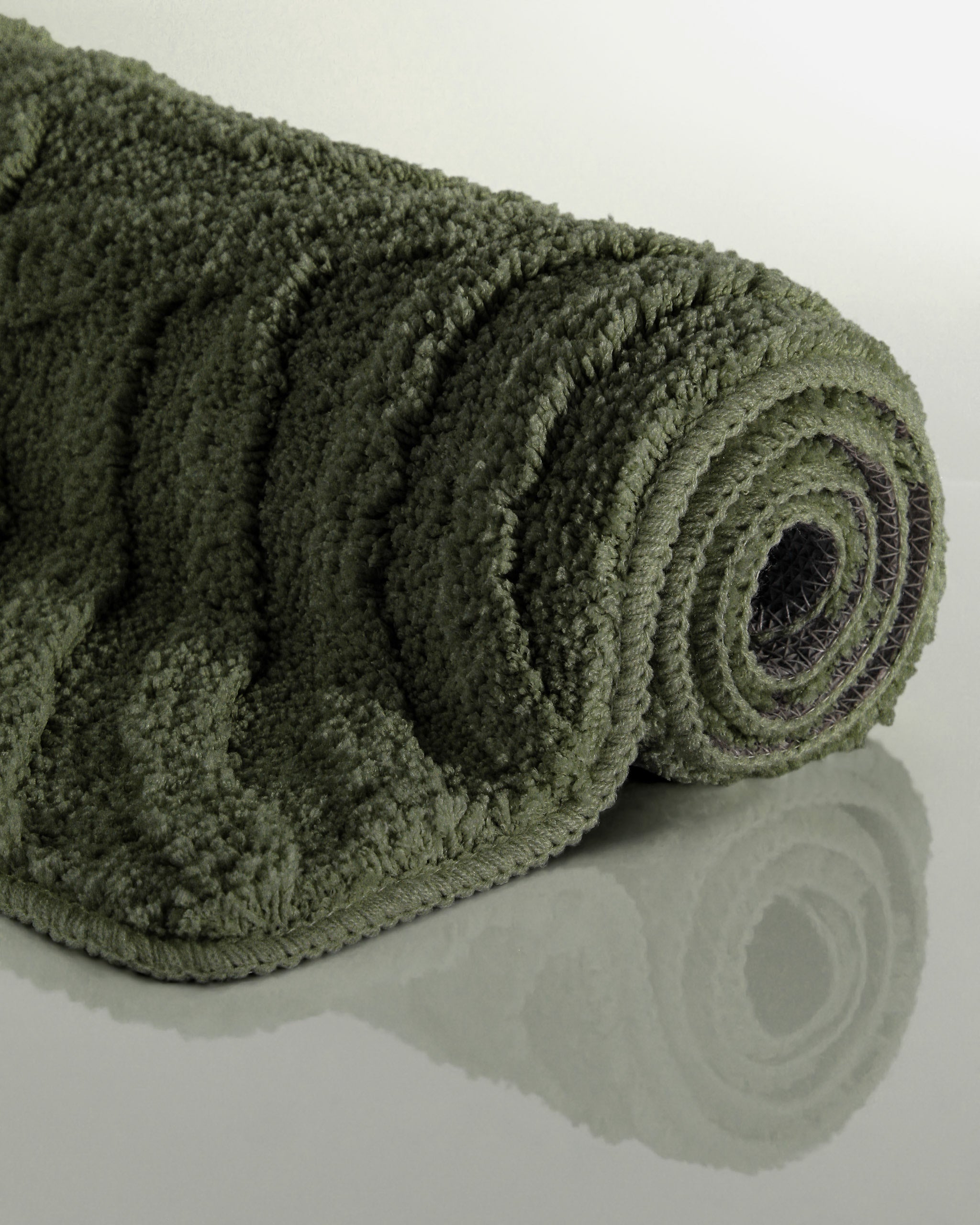 Badteppich von BathKing by WECONhome Fiete Kiefer Grün aufgerollt auf hellem Hintergrund, Seitenansicht zeigt Florhöhe und Teppichkante