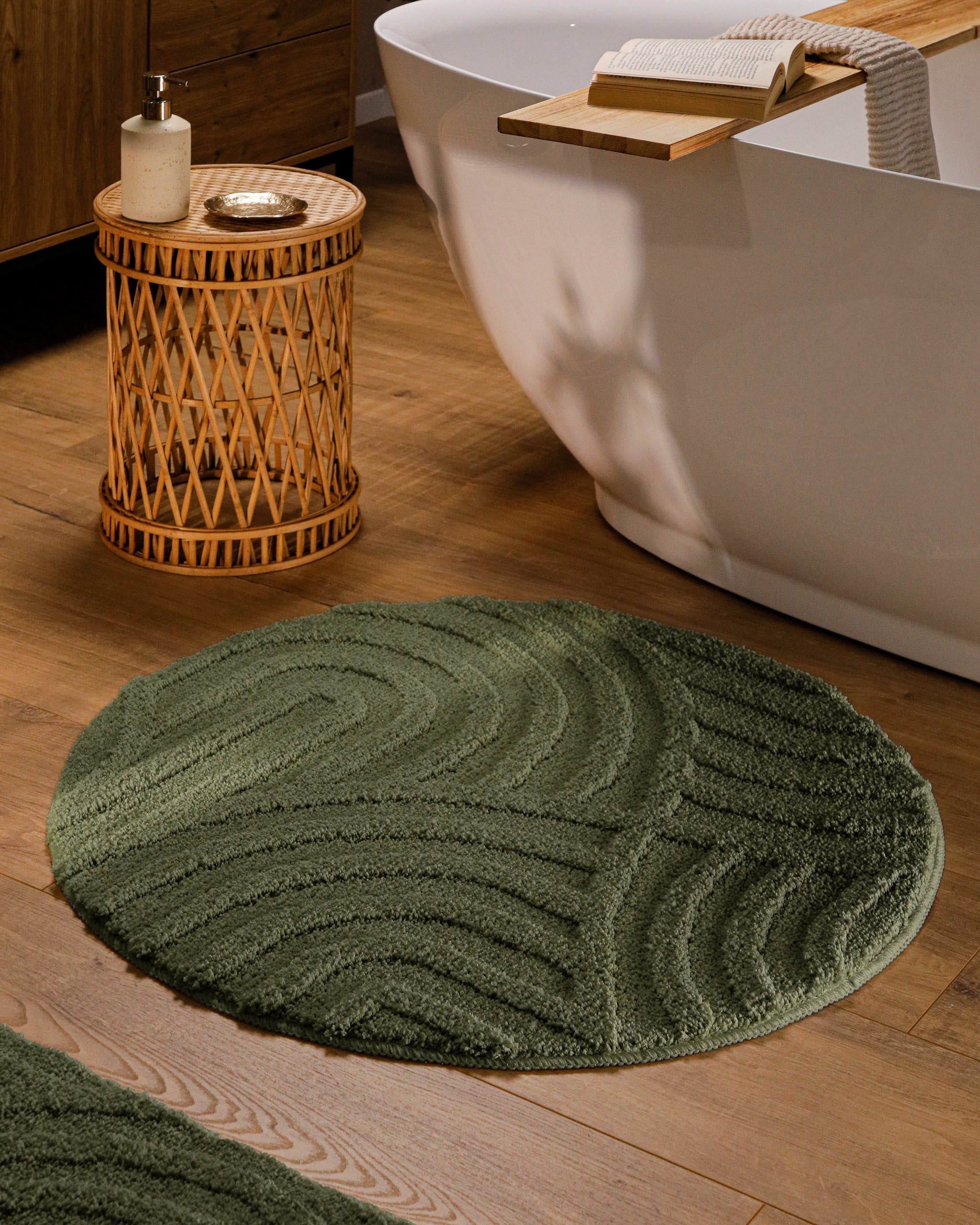 Runder Badteppich von BathKing by WECONhome Fiete Kiefer Grün im Badezimmer vor Badewanne auf Holzboden, strukturiertes Linienrelief im Flor sichtbar
