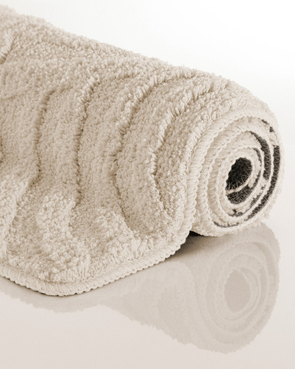 Badteppich von BathKing by WECONhome Fiete Creme Weiß aufgerollt auf hellem Hintergrund, Seitenansicht zeigt Florhöhe und Teppichkante