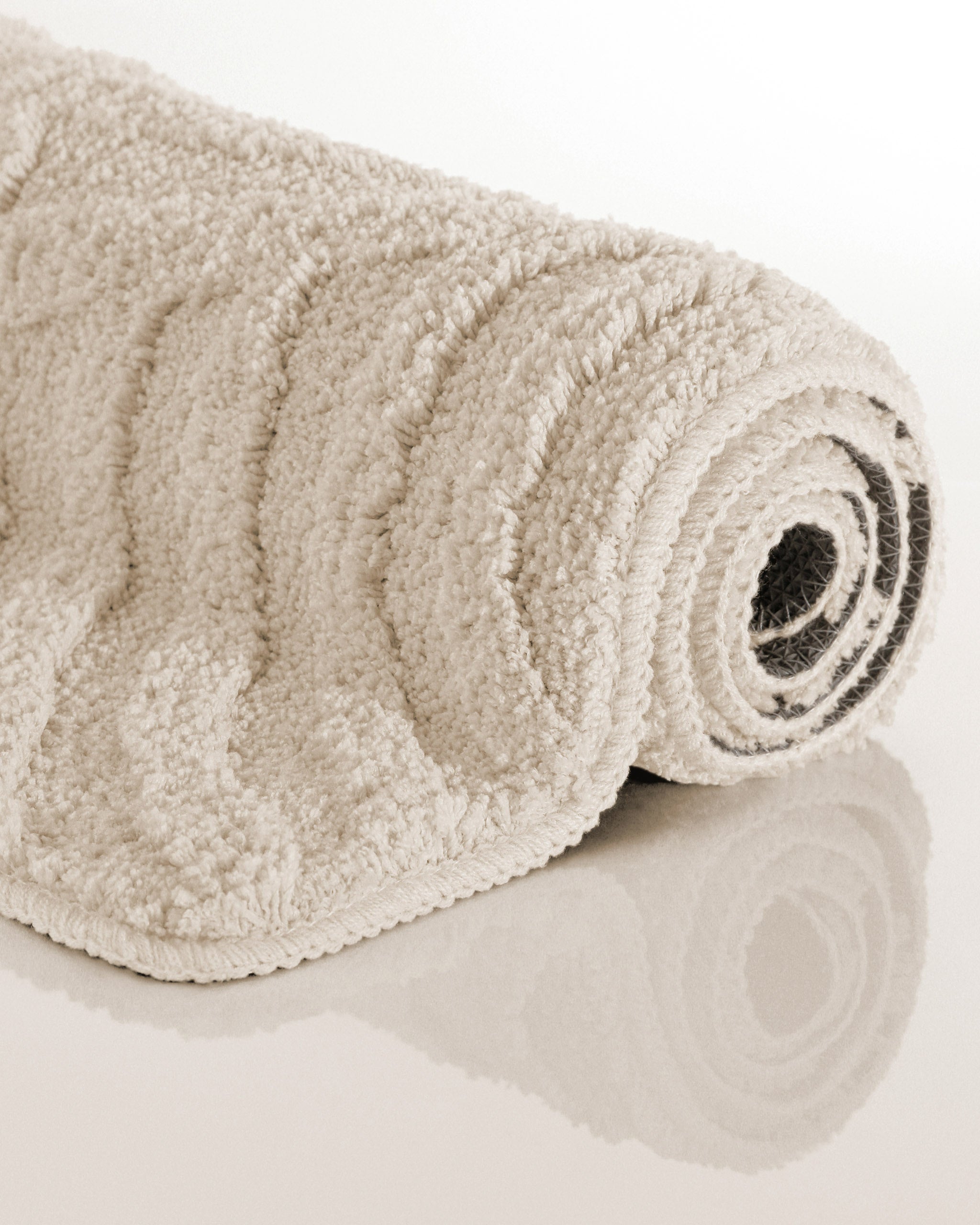 Badteppich von BathKing by WECONhome Fiete Creme Weiß aufgerollt auf hellem Hintergrund, Seitenansicht zeigt Florhöhe und Teppichkante