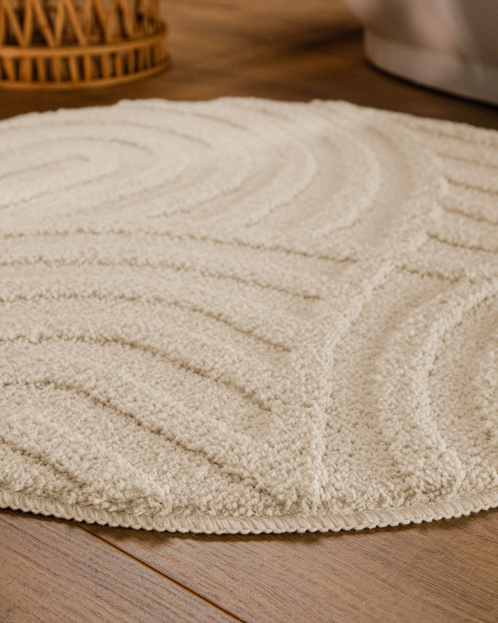 Badteppich von BathKing by WECONhome Fiete Creme Weiß rund im Badezimmer auf Holzboden neben Badewanne, Florstruktur und Linienrelief erkennbar