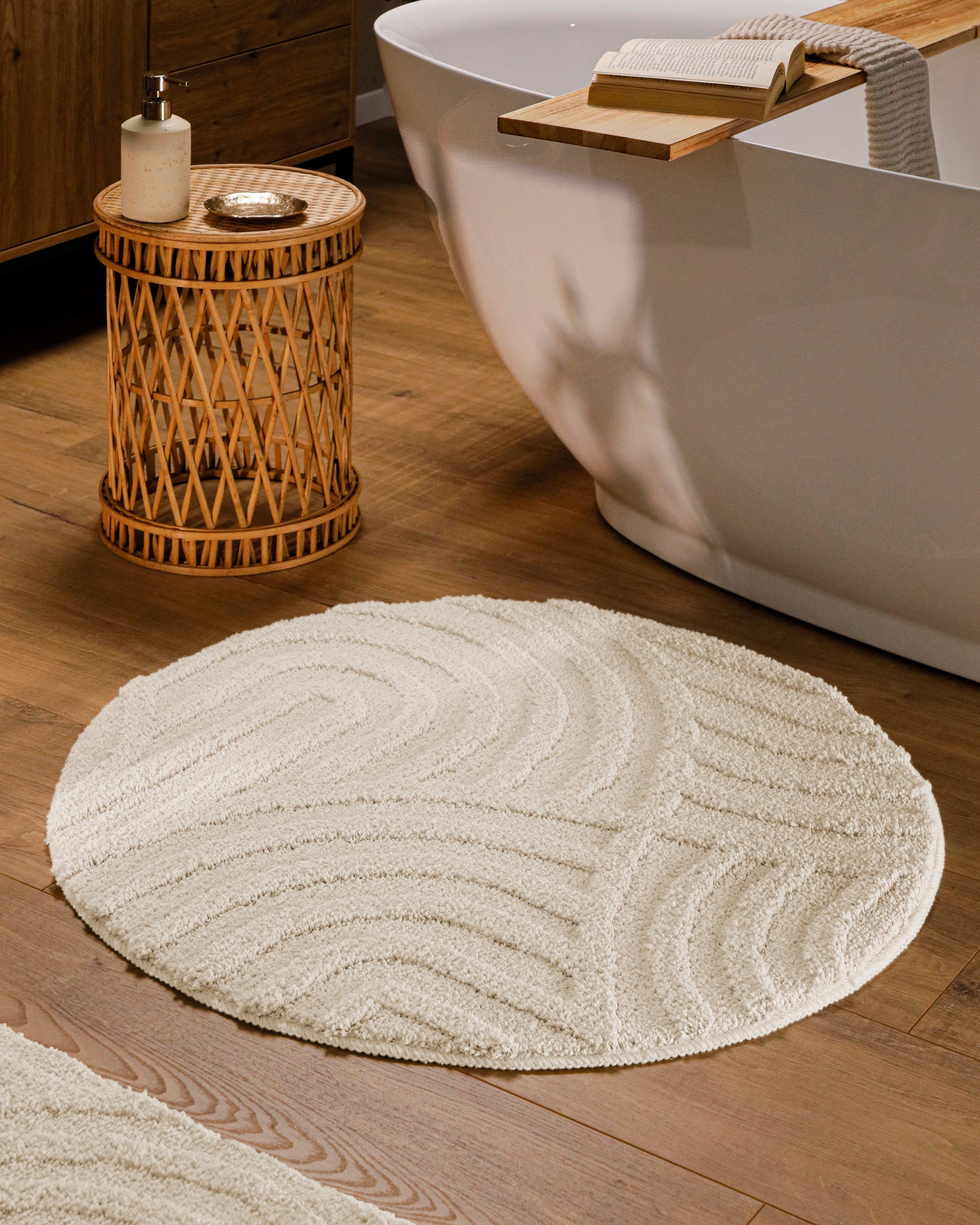 Runder Badteppich von BathKing by WECONhome Fiete Creme Weiß im Badezimmer vor Badewanne auf Holzboden, strukturiertes Linienrelief im Flor sichtbar