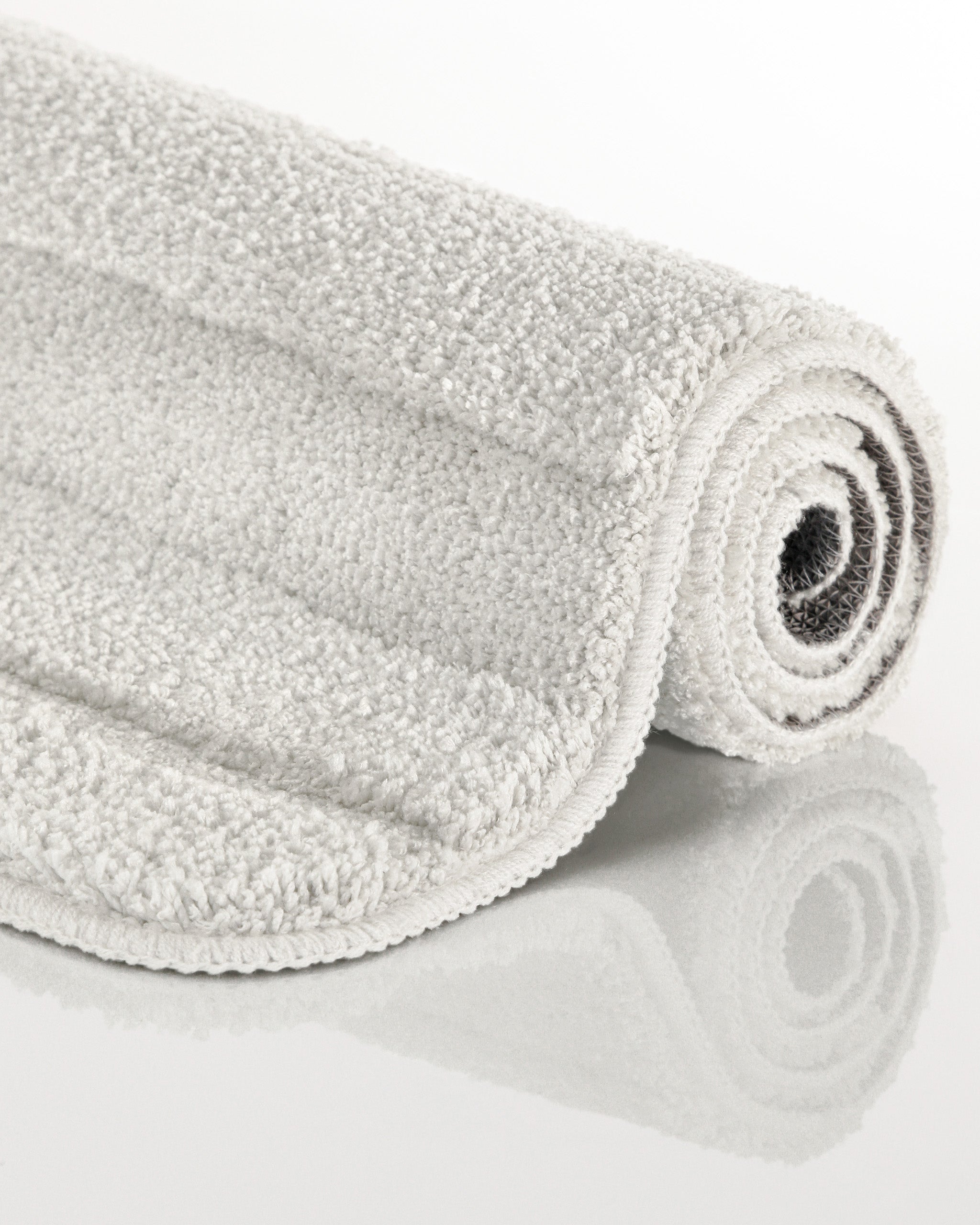 Badteppich von BathKing by WECONhome Marc Weiß aufgerollt auf hellem Hintergrund, Seitenansicht zeigt Florhöhe und Teppichkante