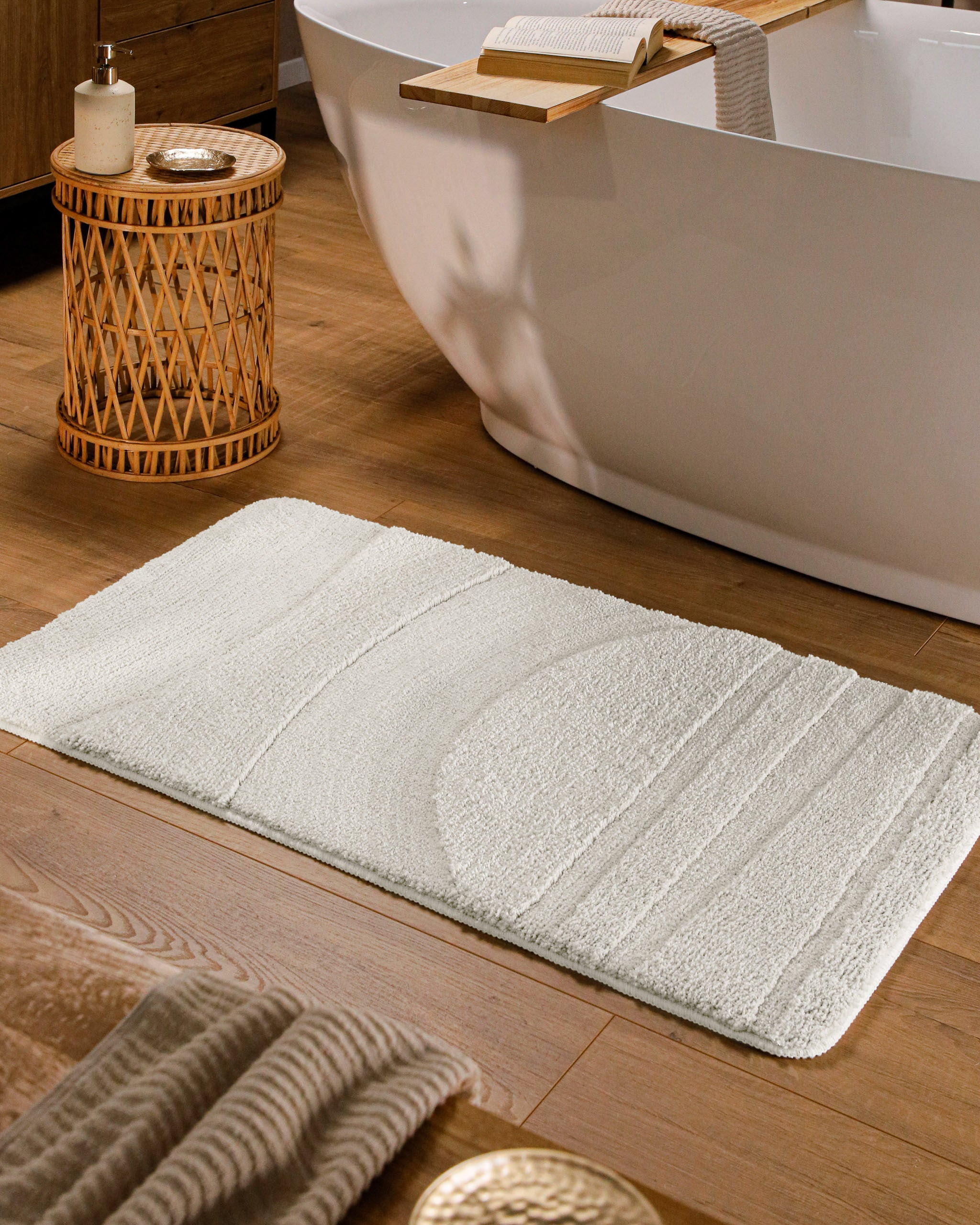 Badteppich von BathKing by WECONhome Marc Weiß rechteckig im Badezimmer vor Badewanne auf Holzboden liegend, Strukturmuster im Flor sichtbar
