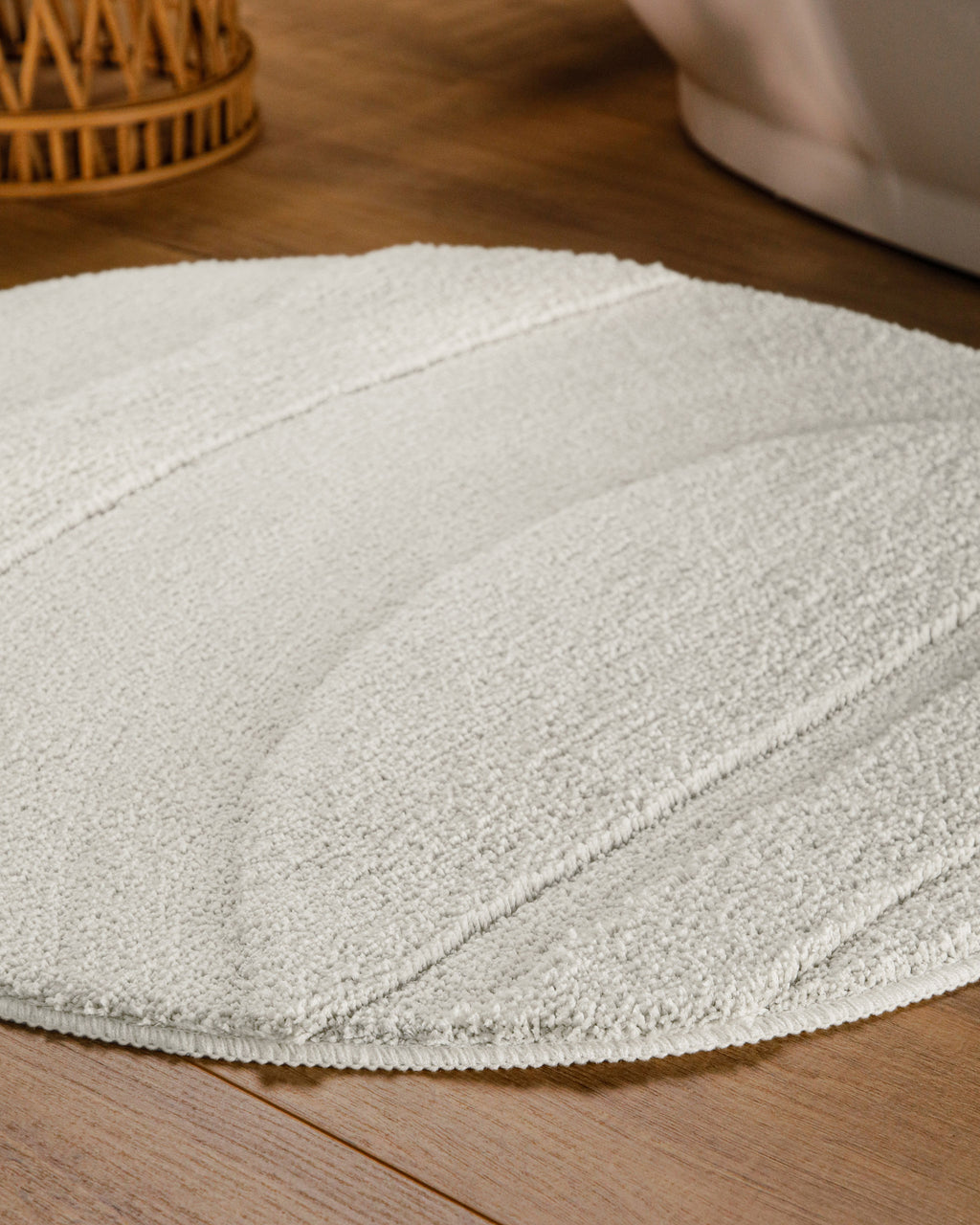 Badteppich von BathKing by WECONhome Marc Weiß rund im Badezimmer auf Holzboden neben Badewanne, Florstruktur und Linienrelief erkennbar
