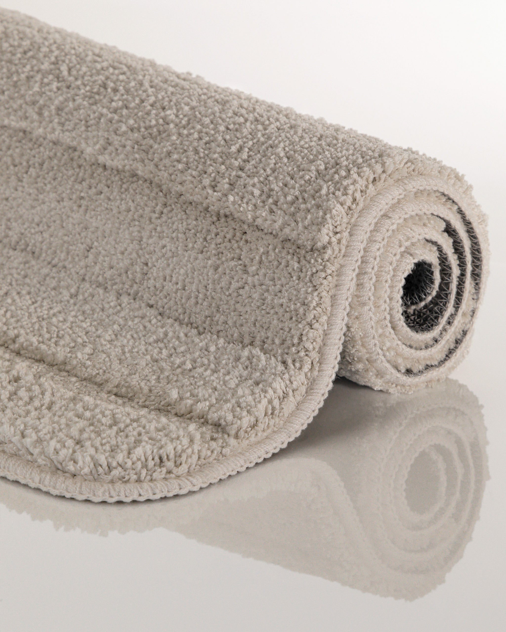 Badteppich von BathKing by WECONhome Marc Grau aufgerollt auf hellem Hintergrund, Seitenansicht zeigt Florhöhe und Teppichkante