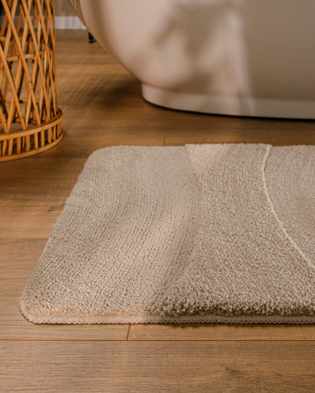 Badteppich von BathKing by WECONhome Marc Sand Beige runde Matte im Badezimmer vor Badewanne, Strukturmuster im Flor auf Holzboden sichtbar