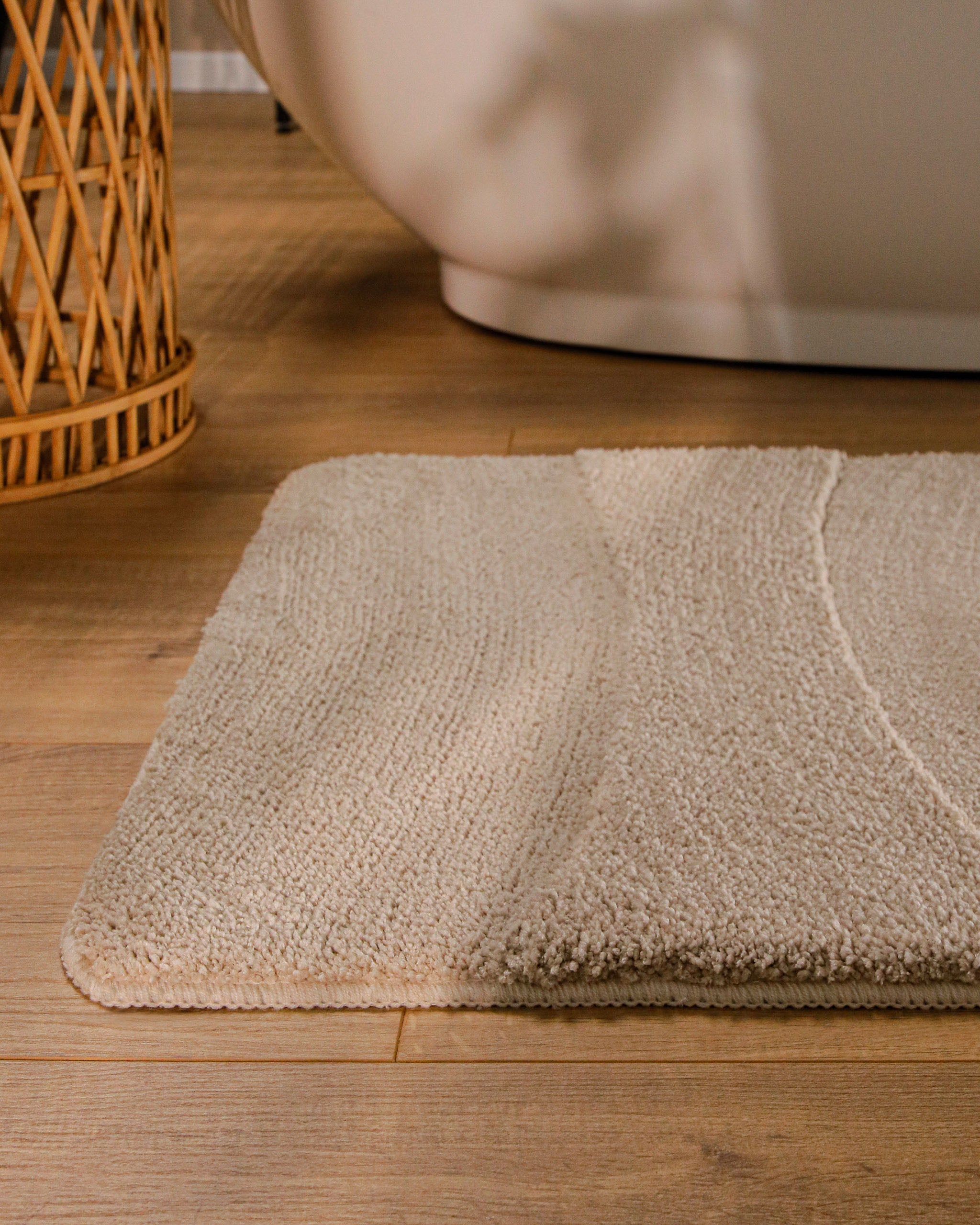Badteppich von BathKing by WECONhome Marc Sand Beige runde Matte im Badezimmer vor Badewanne, Strukturmuster im Flor auf Holzboden sichtbar