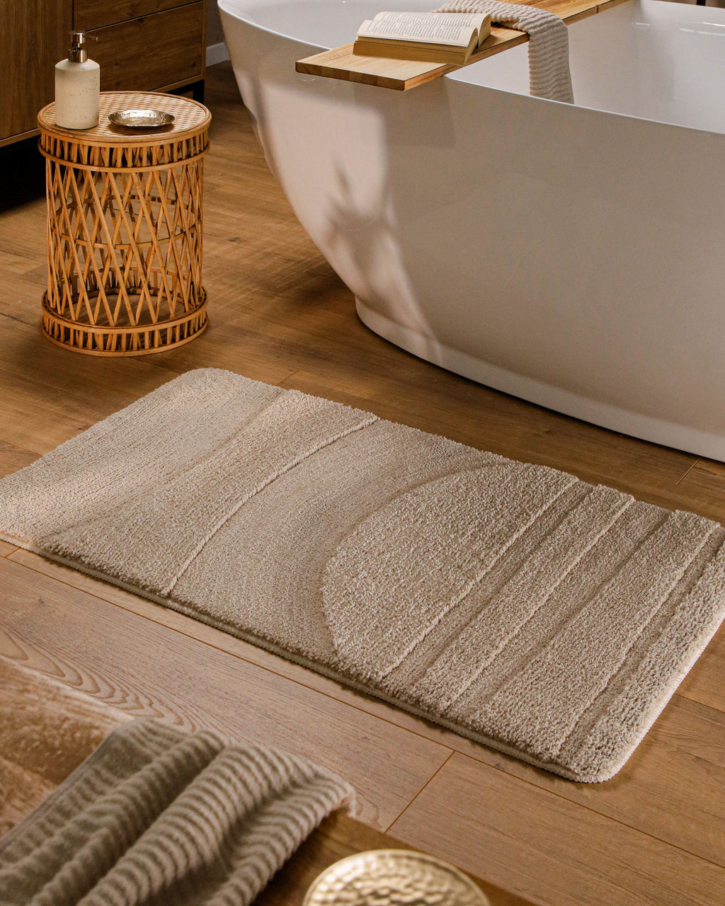 Badteppich von BathKing by WECONhome Marc Sand Beige rechteckig im Badezimmer vor Badewanne auf Holzboden liegend, Strukturmuster im Flor sichtbar