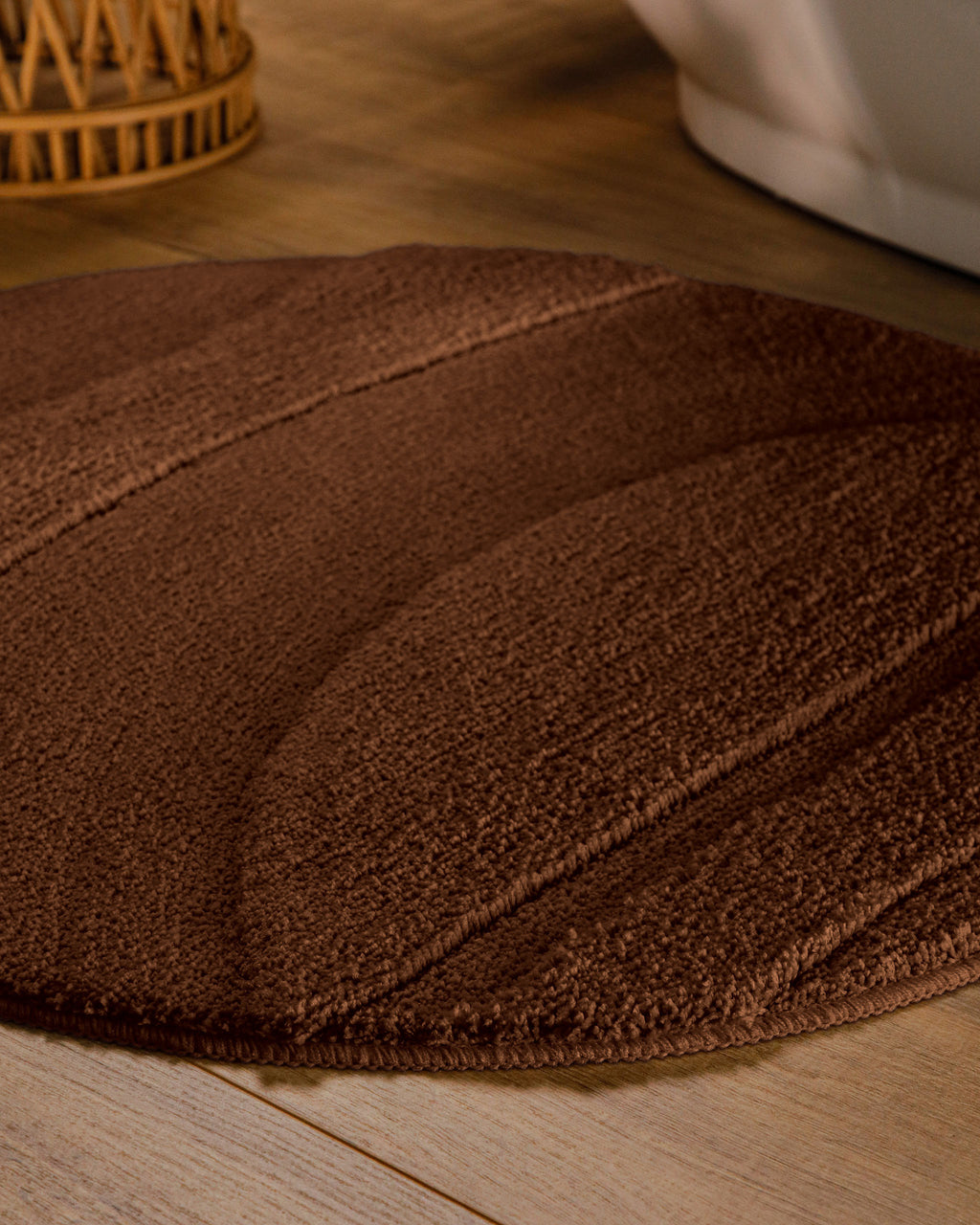 Badteppich von BathKing by WECONhome Marc Braun rund im Badezimmer auf Holzboden neben Badewanne, Florstruktur und Linienrelief erkennbar