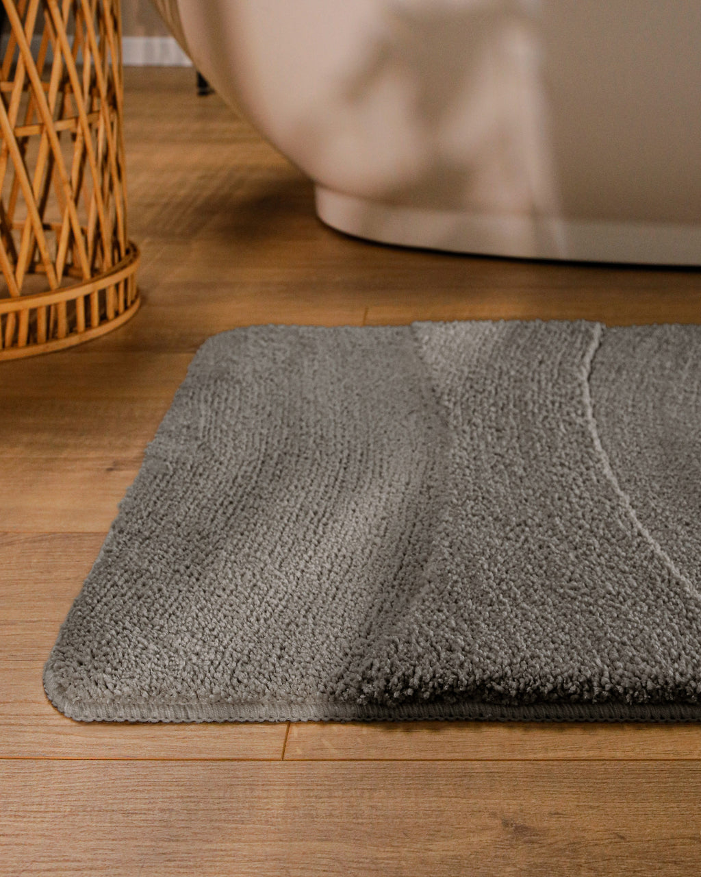 Badteppich von BathKing by WECONhome Marc Basalt Grau runde Matte im Badezimmer vor Badewanne, Strukturmuster im Flor auf Holzboden sichtbar