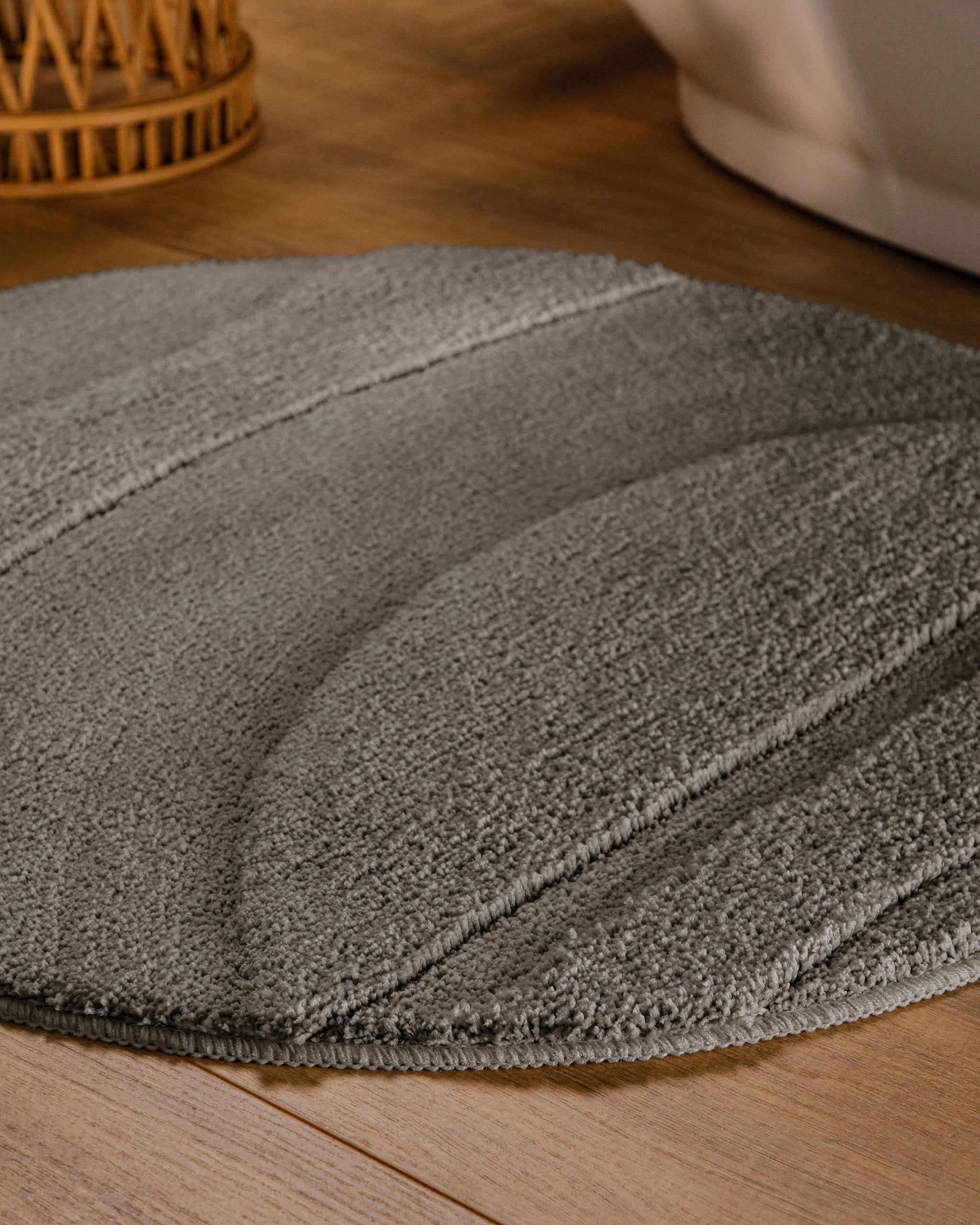 Badteppich von BathKing by WECONhome Marc Basalt Grau rund im Badezimmer auf Holzboden neben Badewanne, Florstruktur und Linienrelief erkennbar