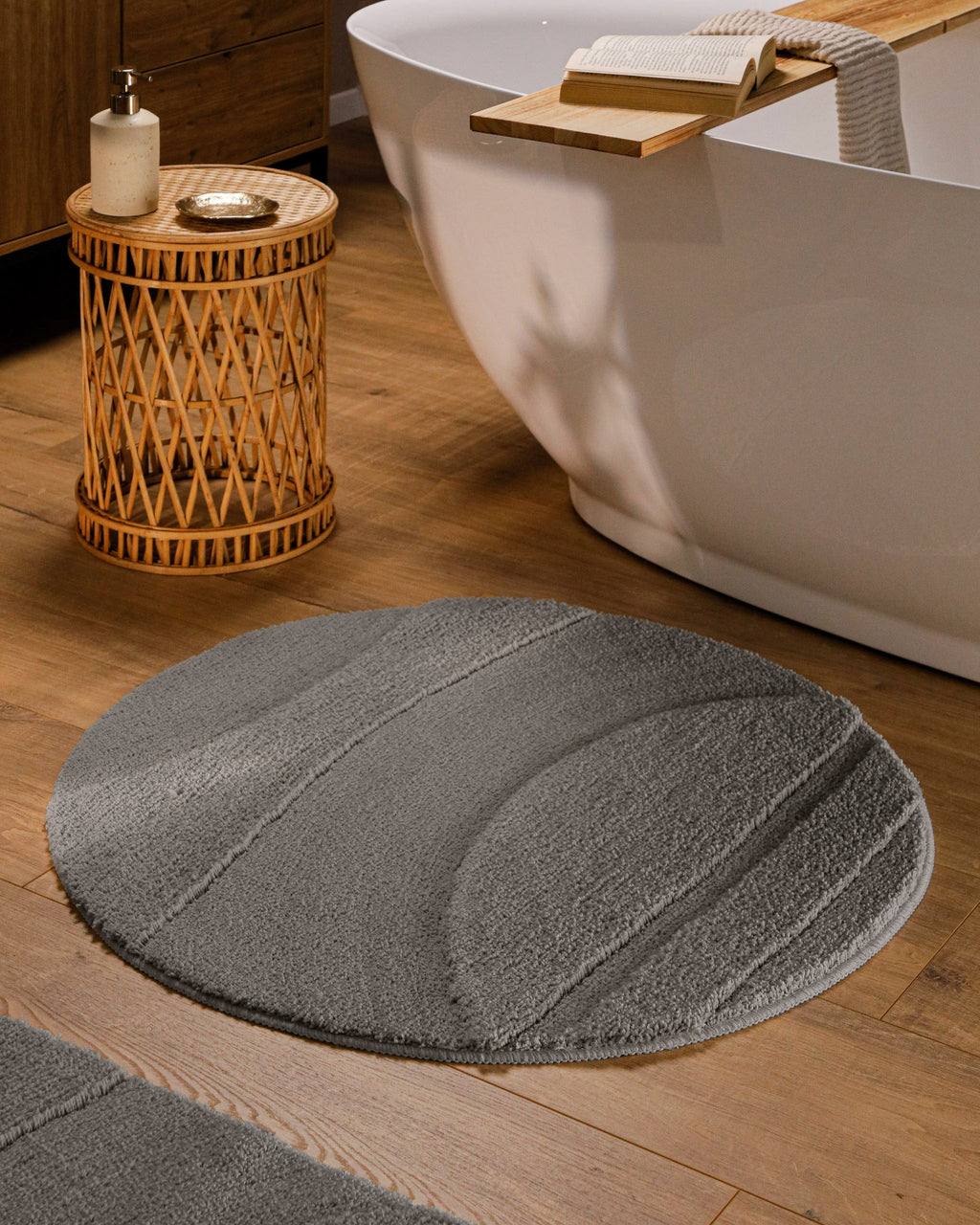 Runder Badteppich von BathKing by WECONhome Marc Basalt Grau im Badezimmer vor Badewanne auf Holzboden, strukturiertes Linienrelief im Flor sichtbar