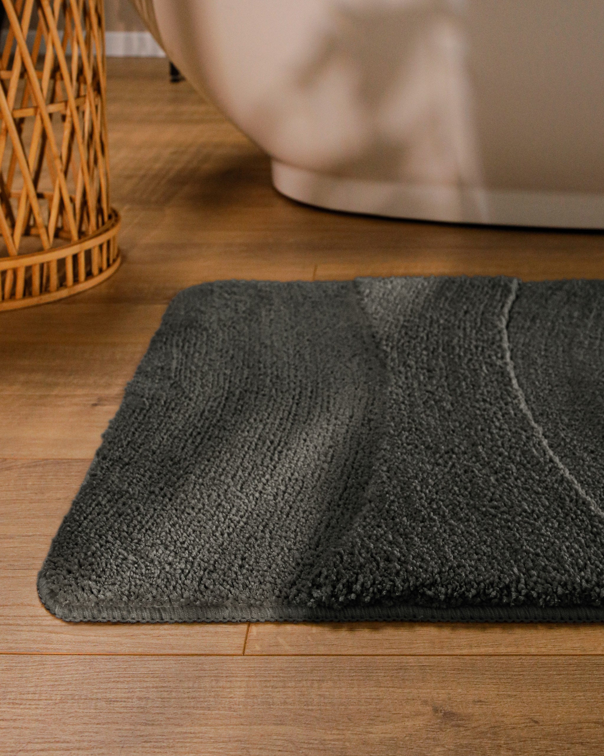 Badteppich von BathKing by WECONhome Marc Anthrazit Grau runde Matte im Badezimmer vor Badewanne, Strukturmuster im Flor auf Holzboden sichtbar