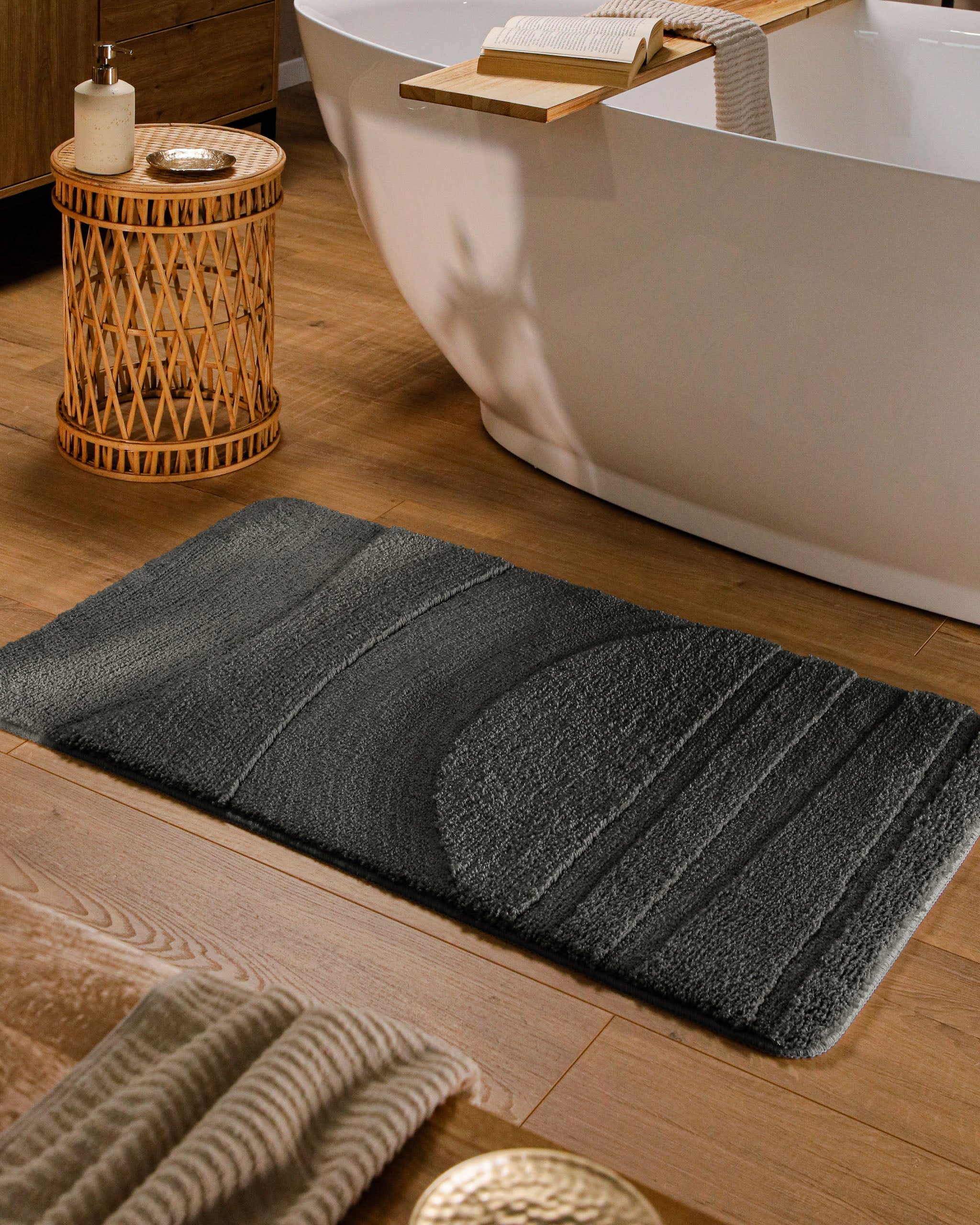 Badteppich von BathKing by WECONhome Marc Anthrazit Grau rechteckig im Badezimmer vor Badewanne auf Holzboden liegend, Strukturmuster im Flor sichtbar